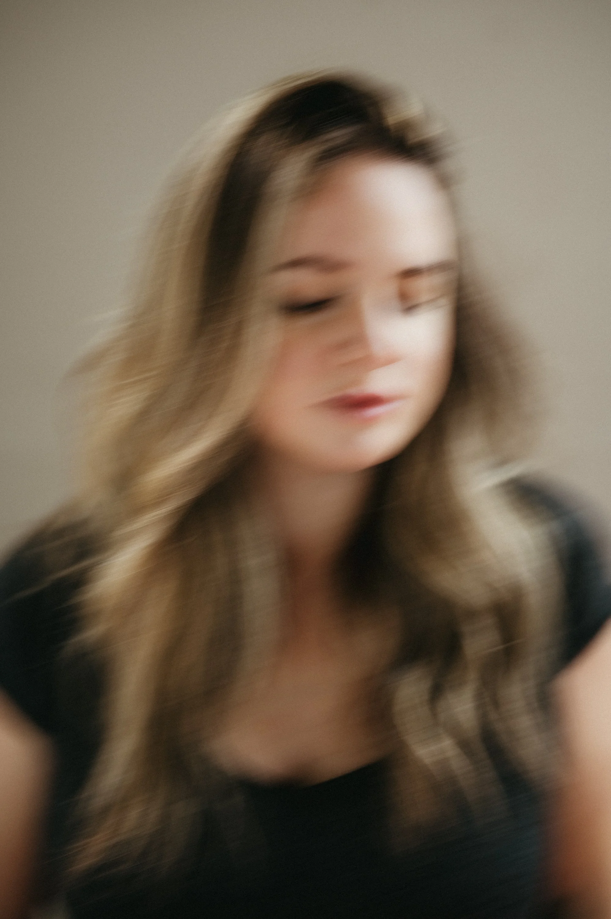 Blurred close-up of a woman with long wavy brown and blonde hair, wearing a black top.