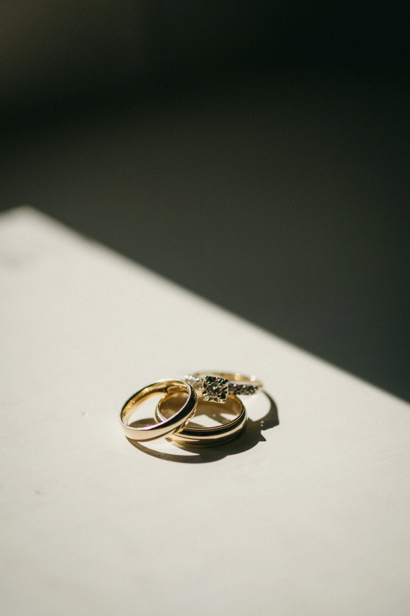 Three gold rings, one with a diamond, resting on a white surface with a shadow.