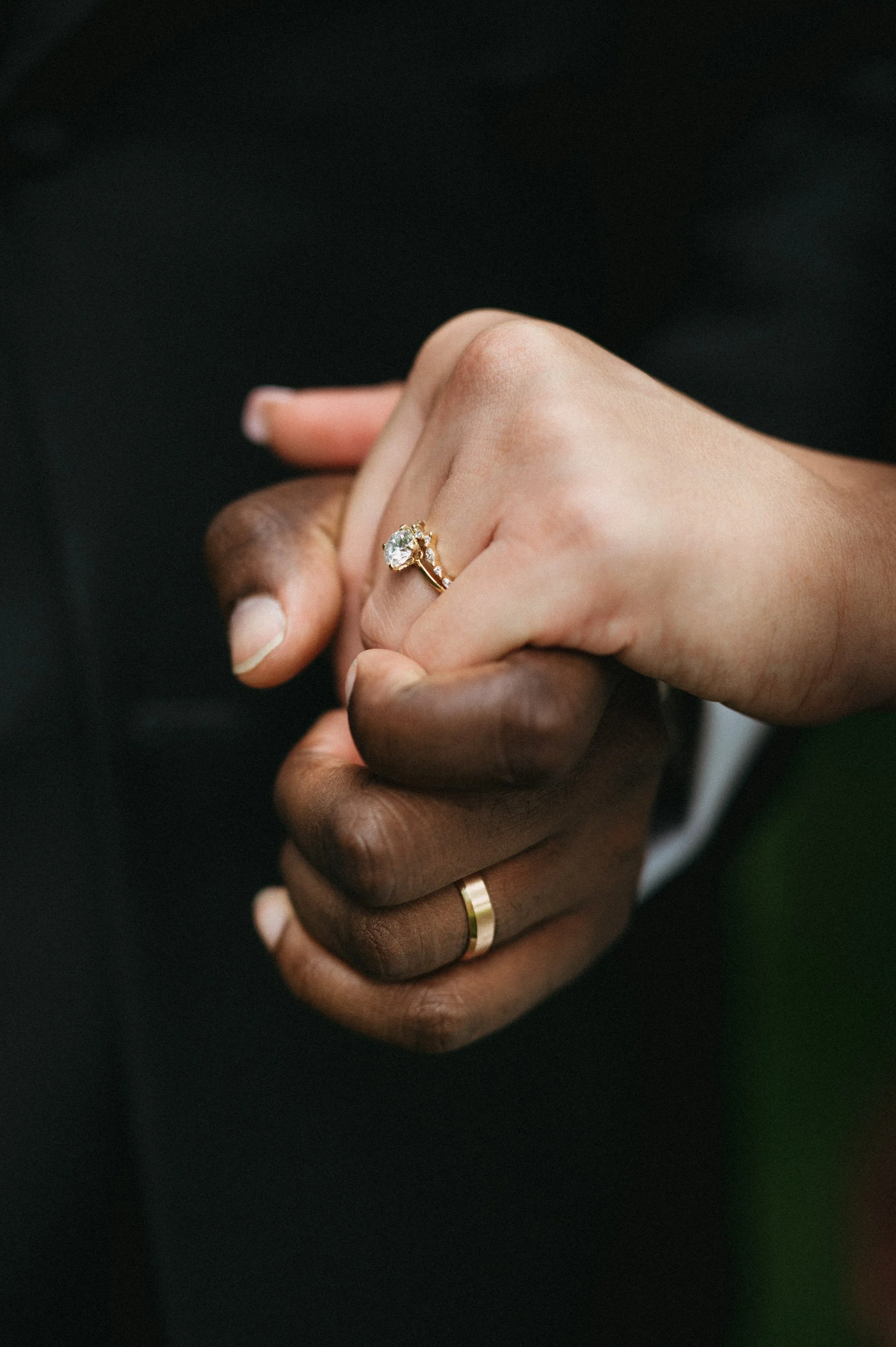 Close-up of a couple holding hands, featuring a diamond engagement ring and a wedding band.