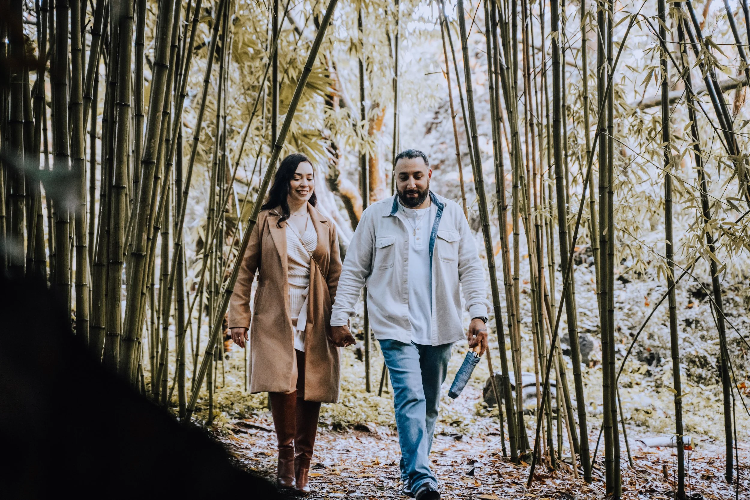 Two people walking through a bamboo forest, holding hands, and smiling.