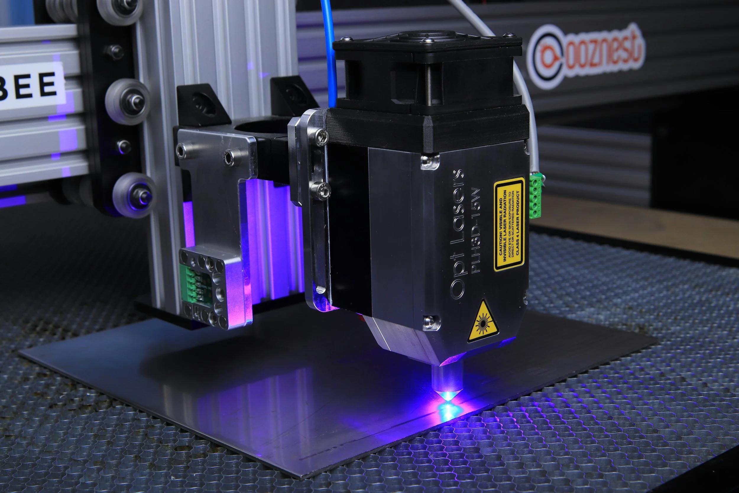 A laser engraving machine marking a surface with blue laser light, placed on a metal worktable.