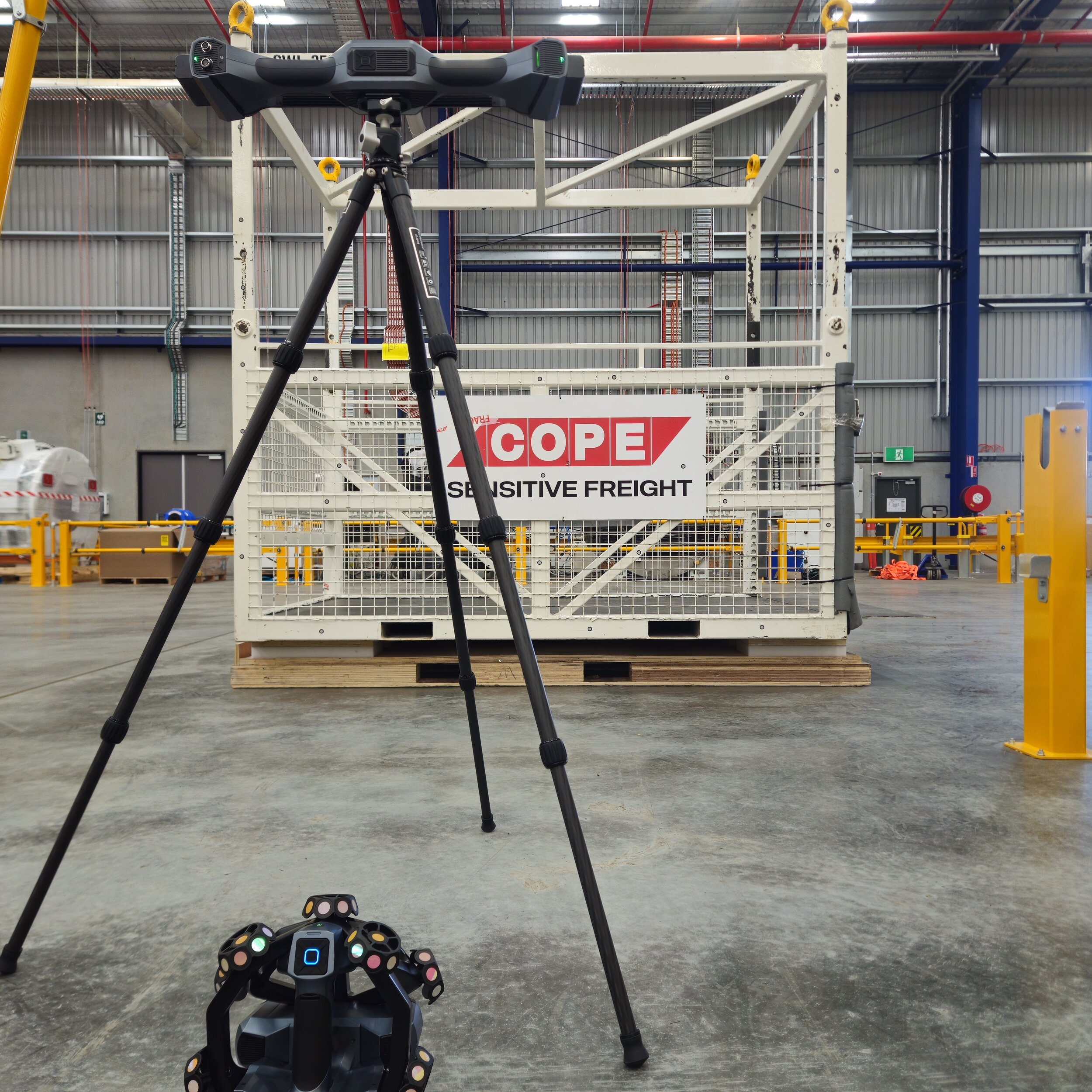 A freight container on a pallet inside a warehouse, with a tripod and camera setup in front of it, and a sign reading 'COPE Sensitive Freight' on the container.