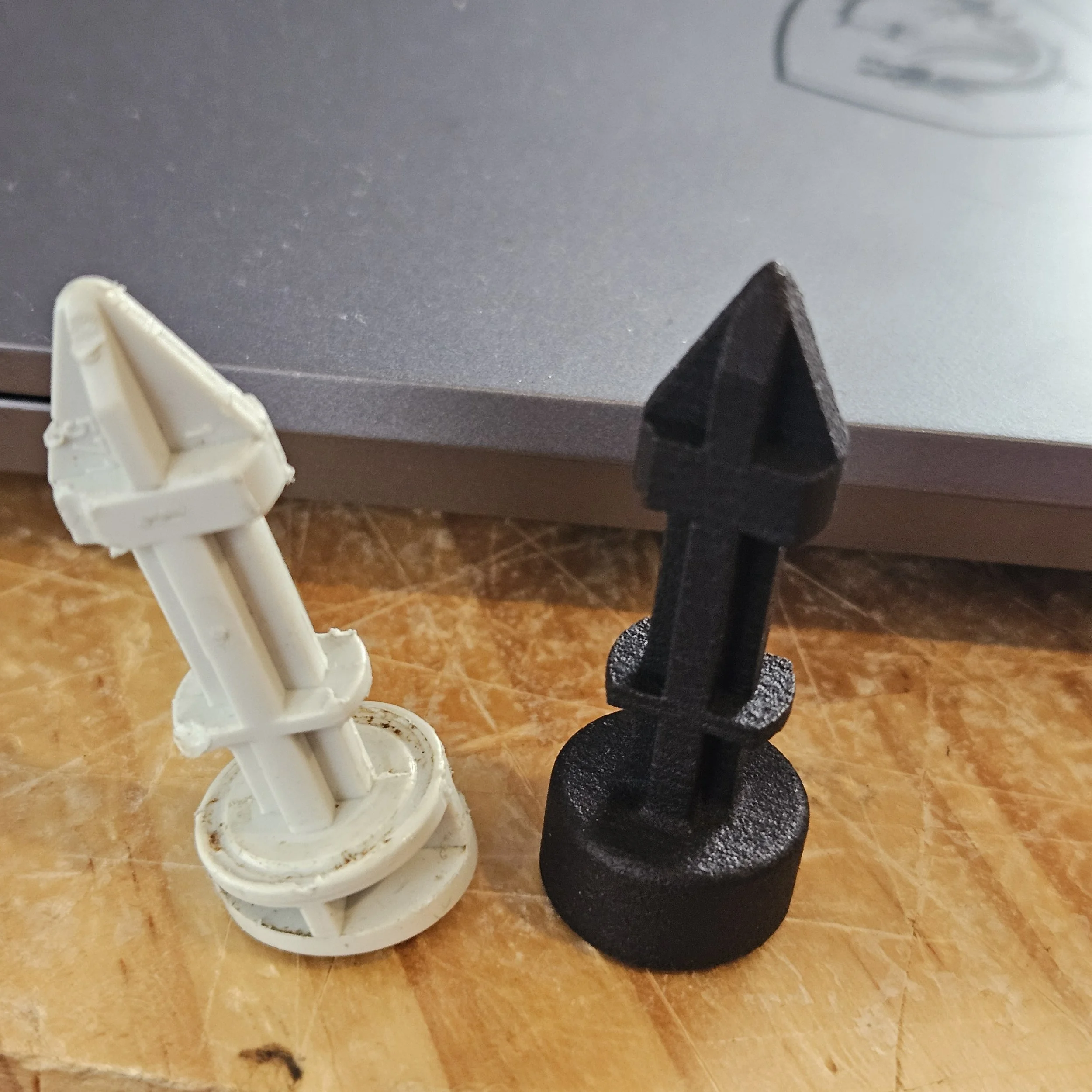 Two plastic game pieces designed to resemble missiles, one white and one black, standing upright on a wooden surface with a silver laptop in the background.