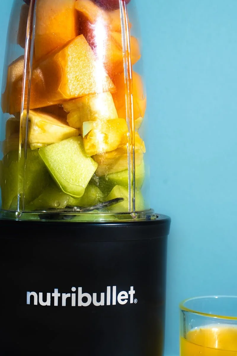 nutri bullet with layered fruit on blue background, orange juice