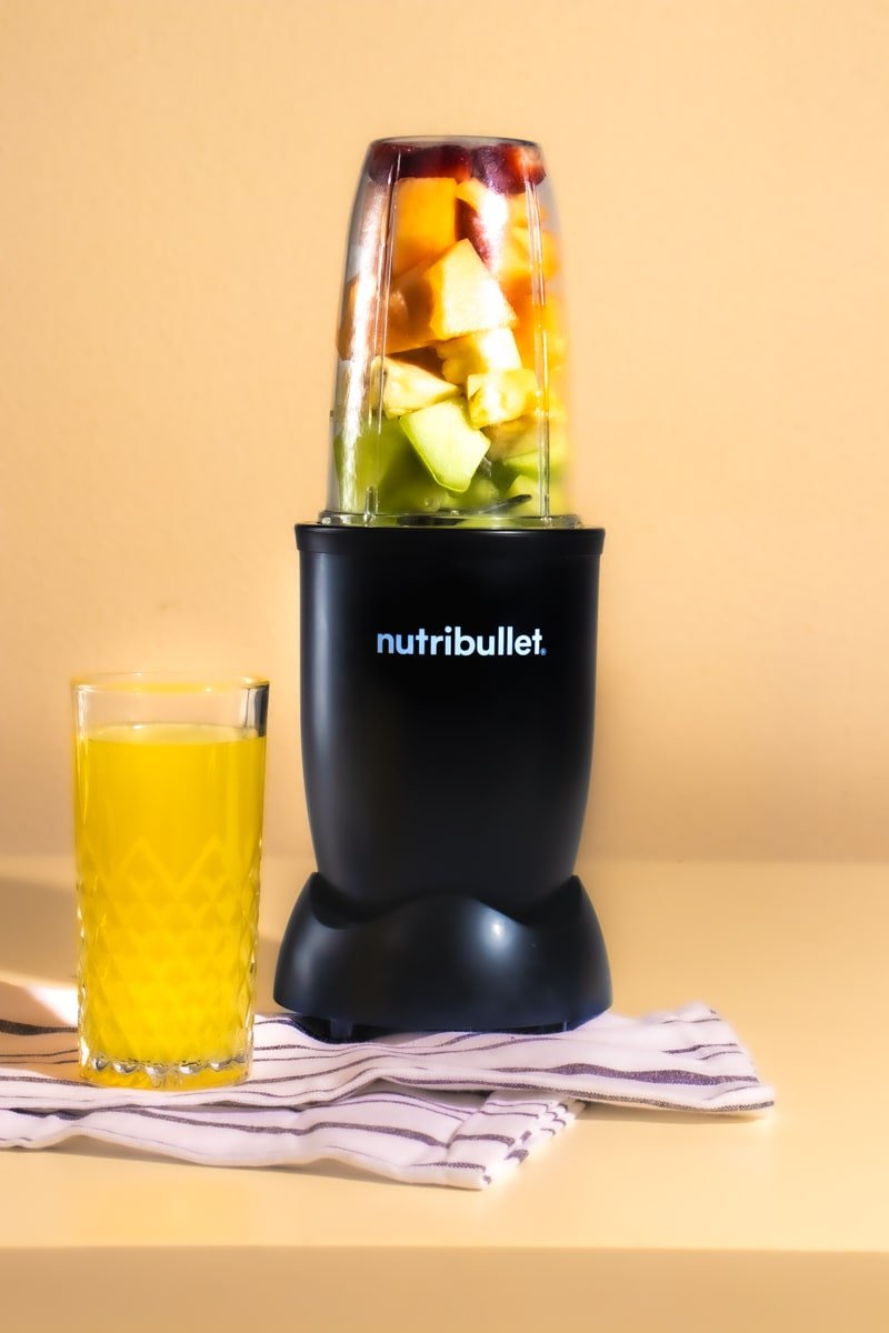 nutri bullet with layered fruit on cream, background, orange juice, and white stripped hand towel