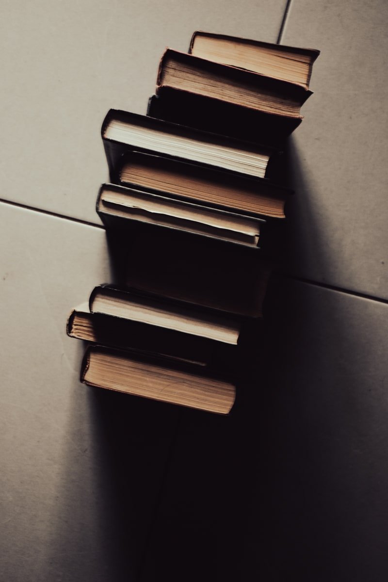 stacked books across tiled building floor. shadow cast across floor creating a gloomy effect