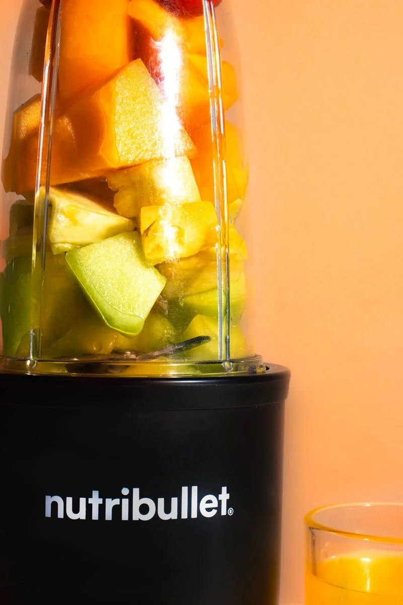 nutri bullet with layered fruit on orange background, orange juice