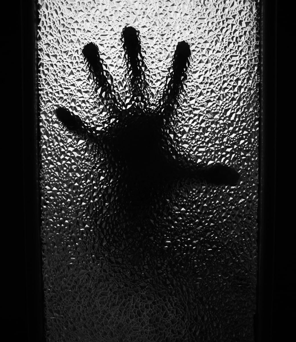 shadow of hand grasping at mosaic window. confined by the window frame looks like it is trying to escape