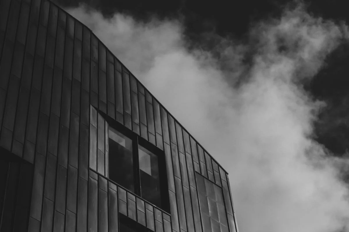 Close-up of a modern building with dark, square tiles and large window against a cloudy sky.