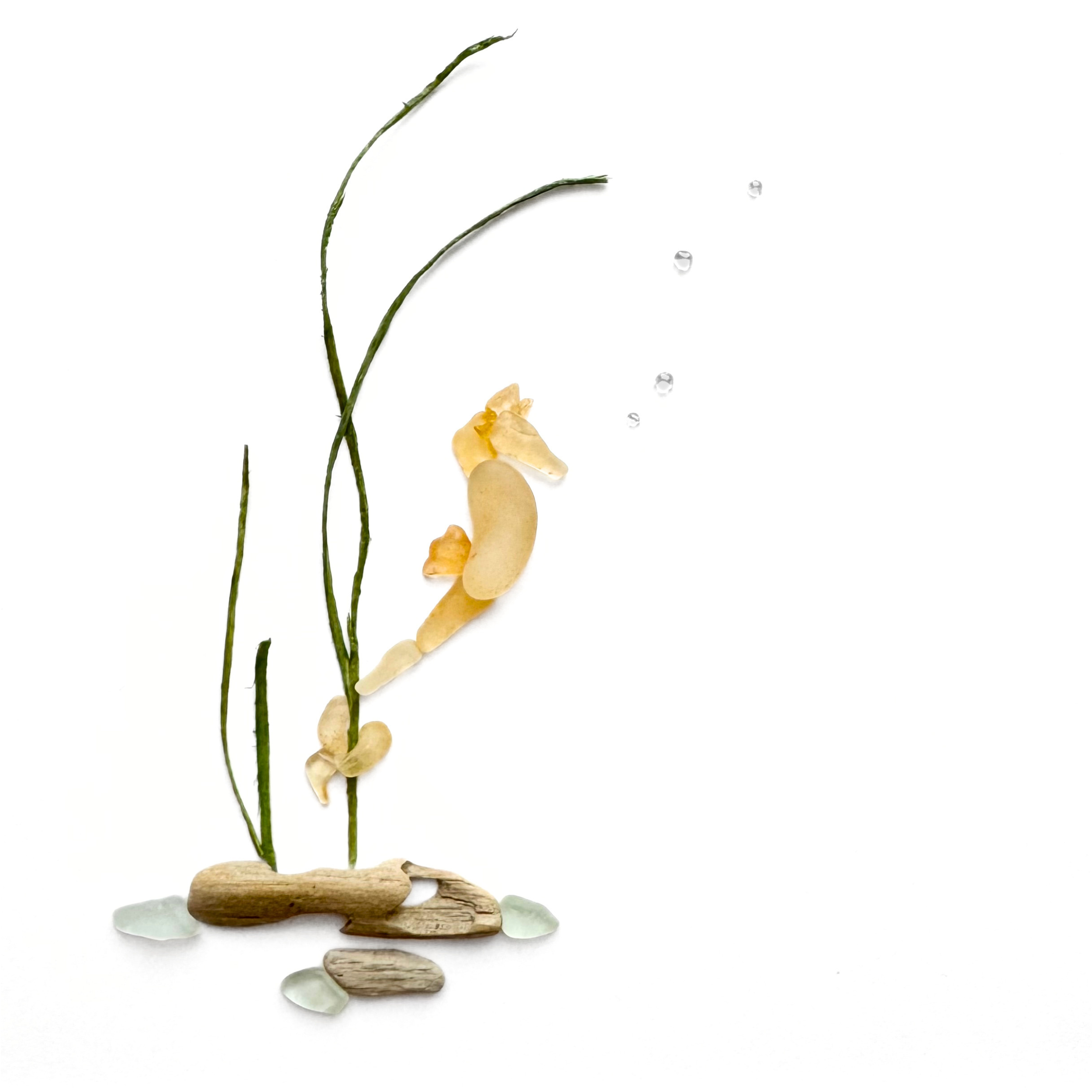 Yellow sea glass seahorse floating among preserved seagrass and beach stones.