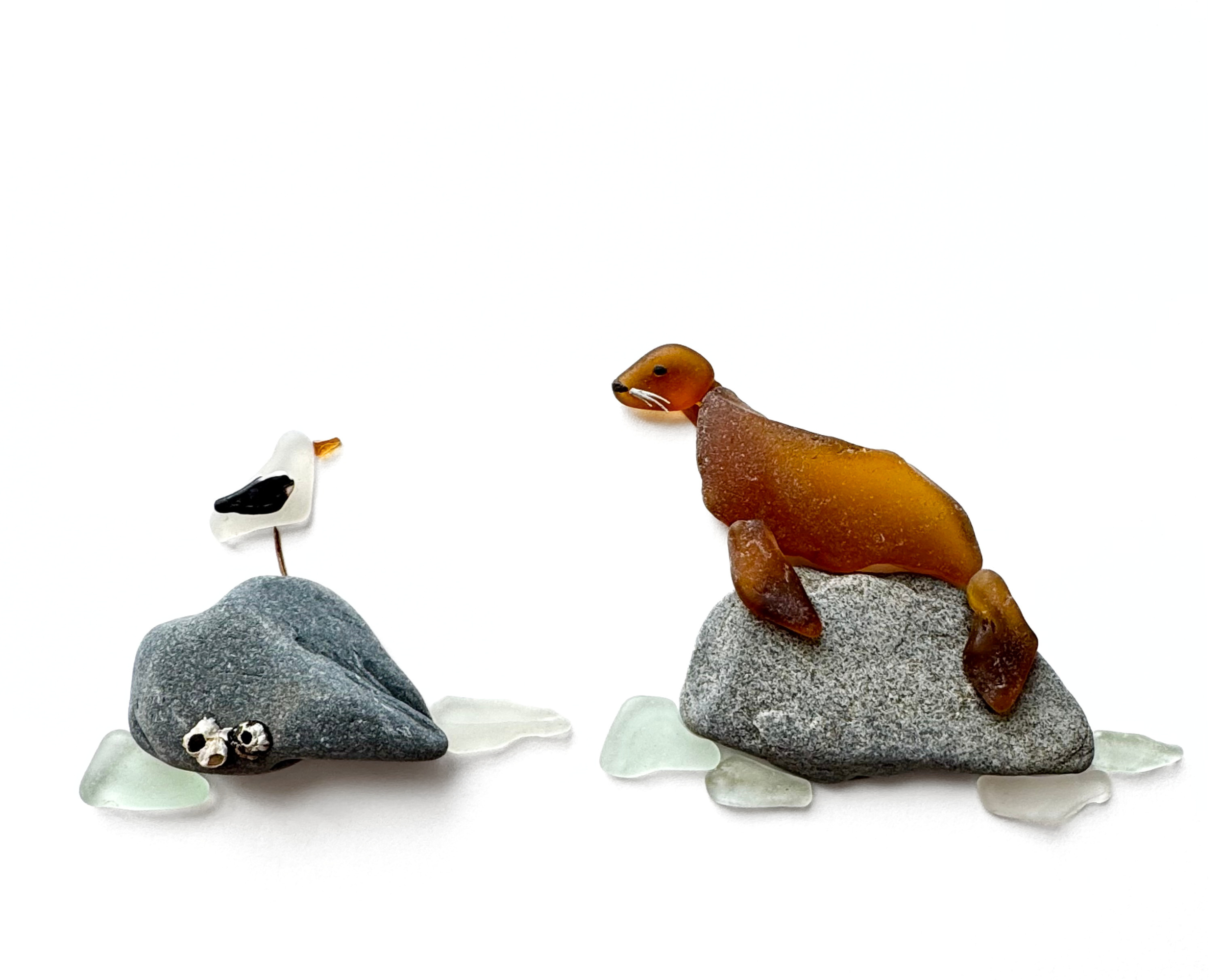 Sea lion and seagull perched on coastal rocks, created with naturally shaped sea glass, beach stones, and tiny barnacle details.