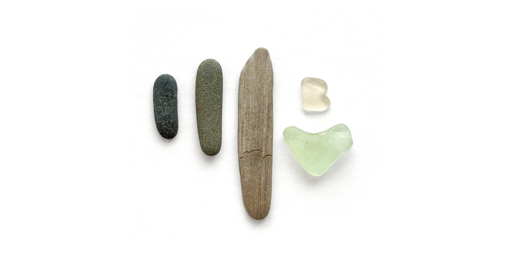 Sea glass pieces and driftwood arranged to form the letter B on a white background, representing B.Found Sea Glass.