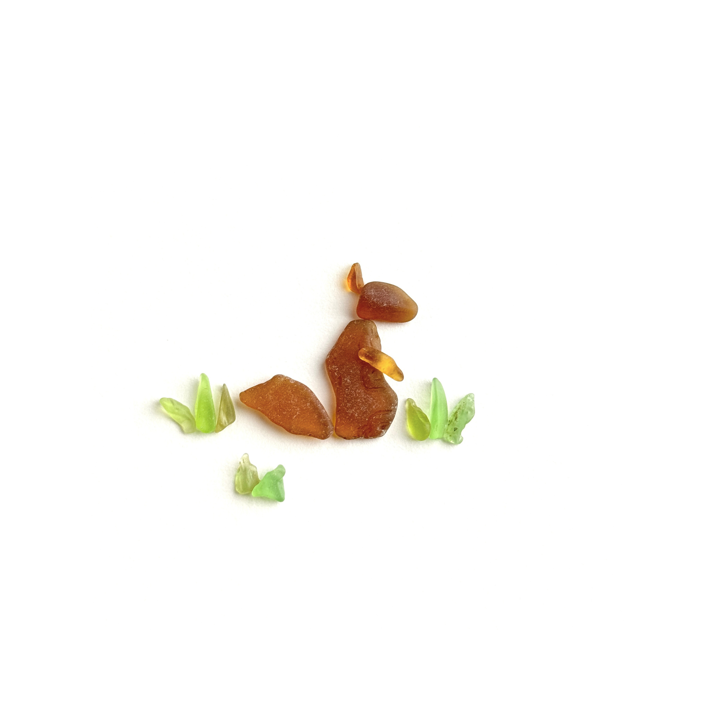 A small sea glass squirrel pauses in the grass, alert to the woodland world around it.