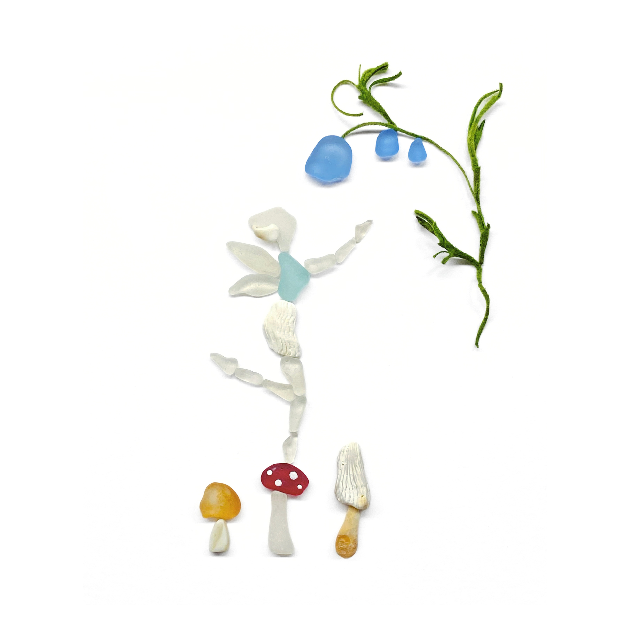 An ethereal woodland fairy appears among blue flowers, curling vines, and tiny mushrooms created from sea glass and beachcombed treasures.