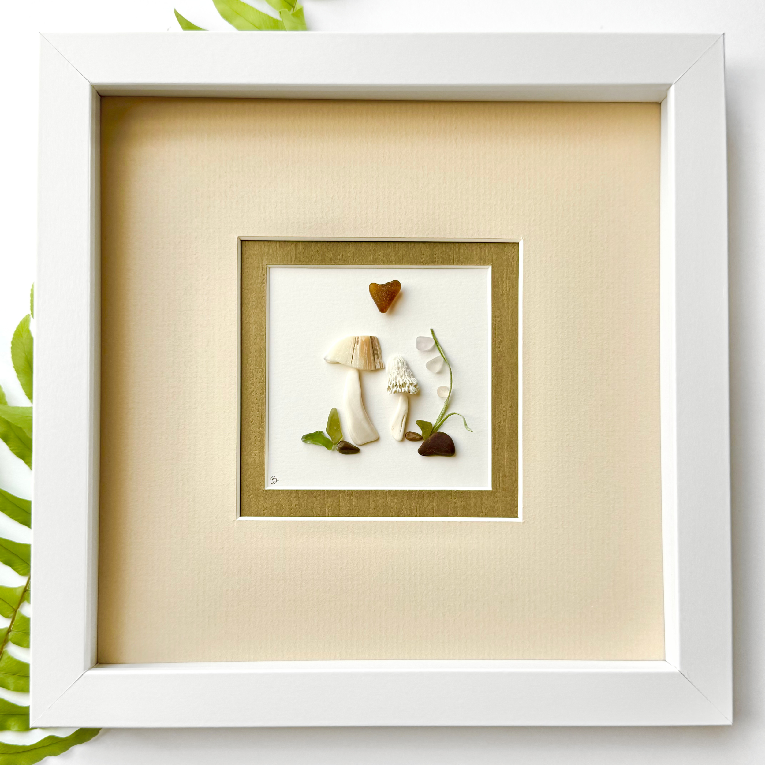 A framed woodland mushroom garden created with sea glass, shells, beach stones, and naturally found materials.