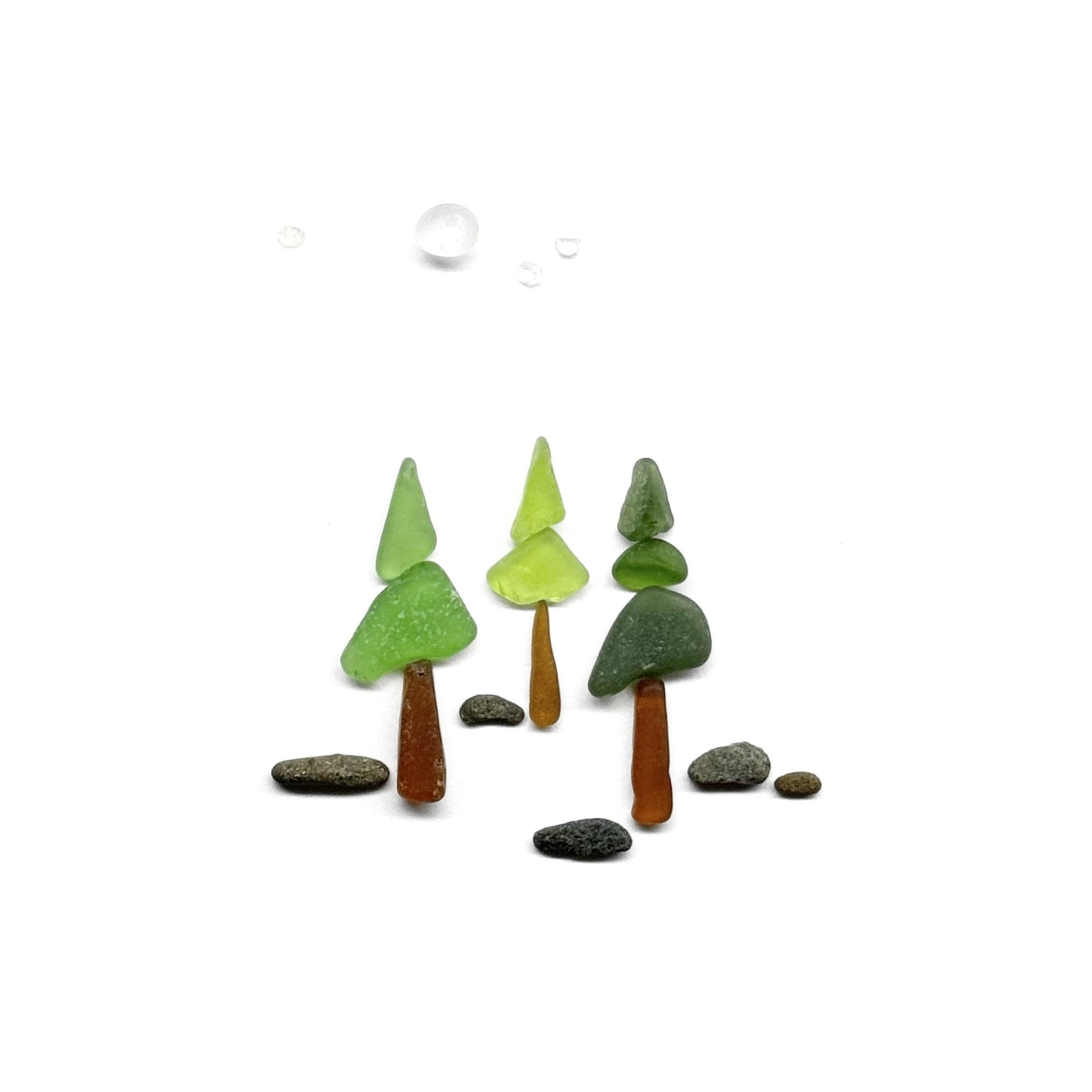 Three miniature evergreen trees created with green and amber sea glass stand beneath a softly glowing moon.