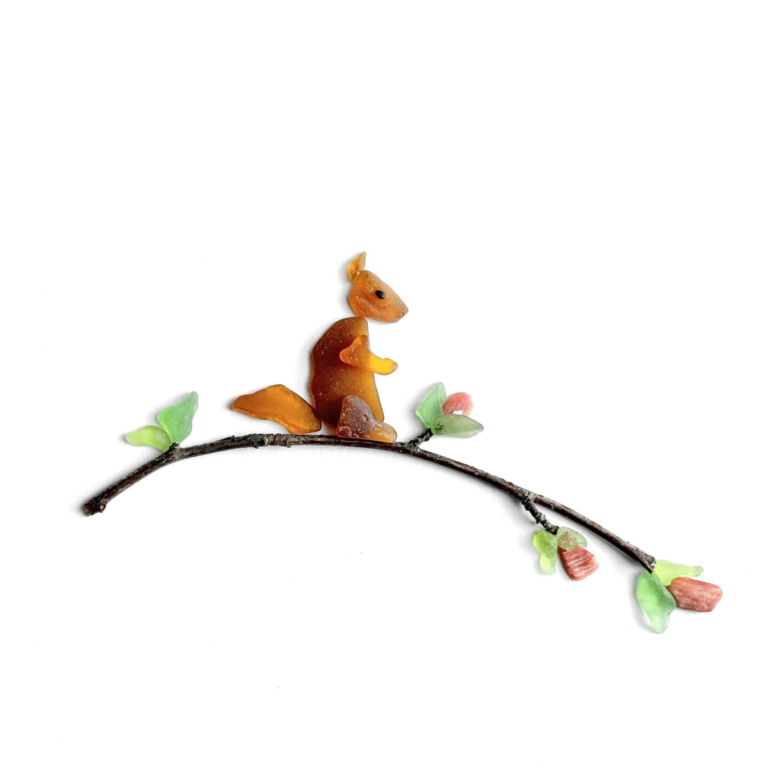 A sea glass chipmunk rests on a slender flowering branch surrounded by fresh green leaves.