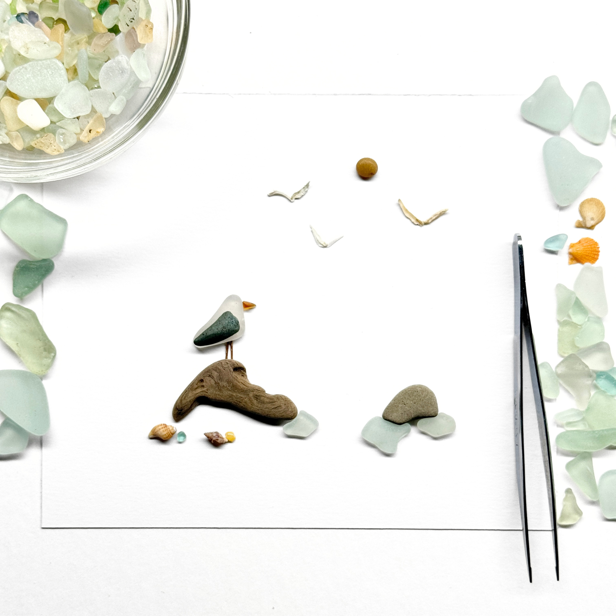 Behind-the-scenes view of a coastal sea glass artwork in progress, with beach-found materials awaiting placement.