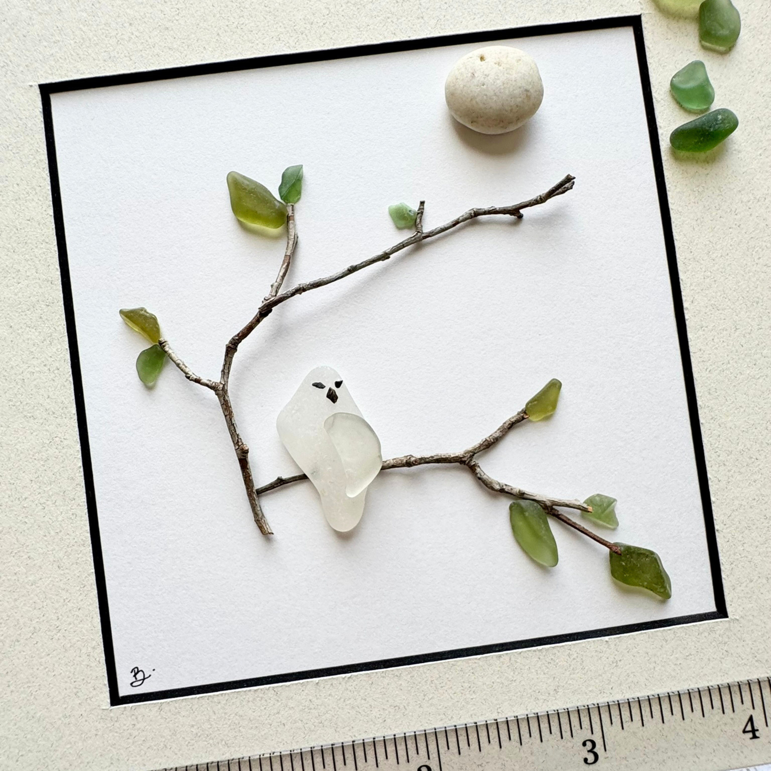 A behind-the-scenes look at a sea glass owl taking shape among natural branches and leaves.