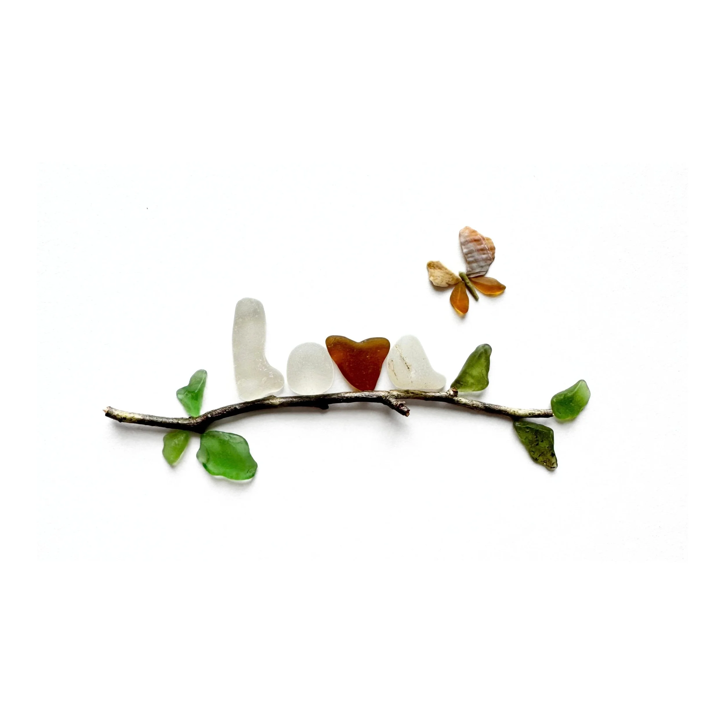 Original sea glass artwork featuring the word LOVE spelled out in pale sea glass, with an amber heart at its center, a leafy branch, and a golden butterfly hovering above against a white background.