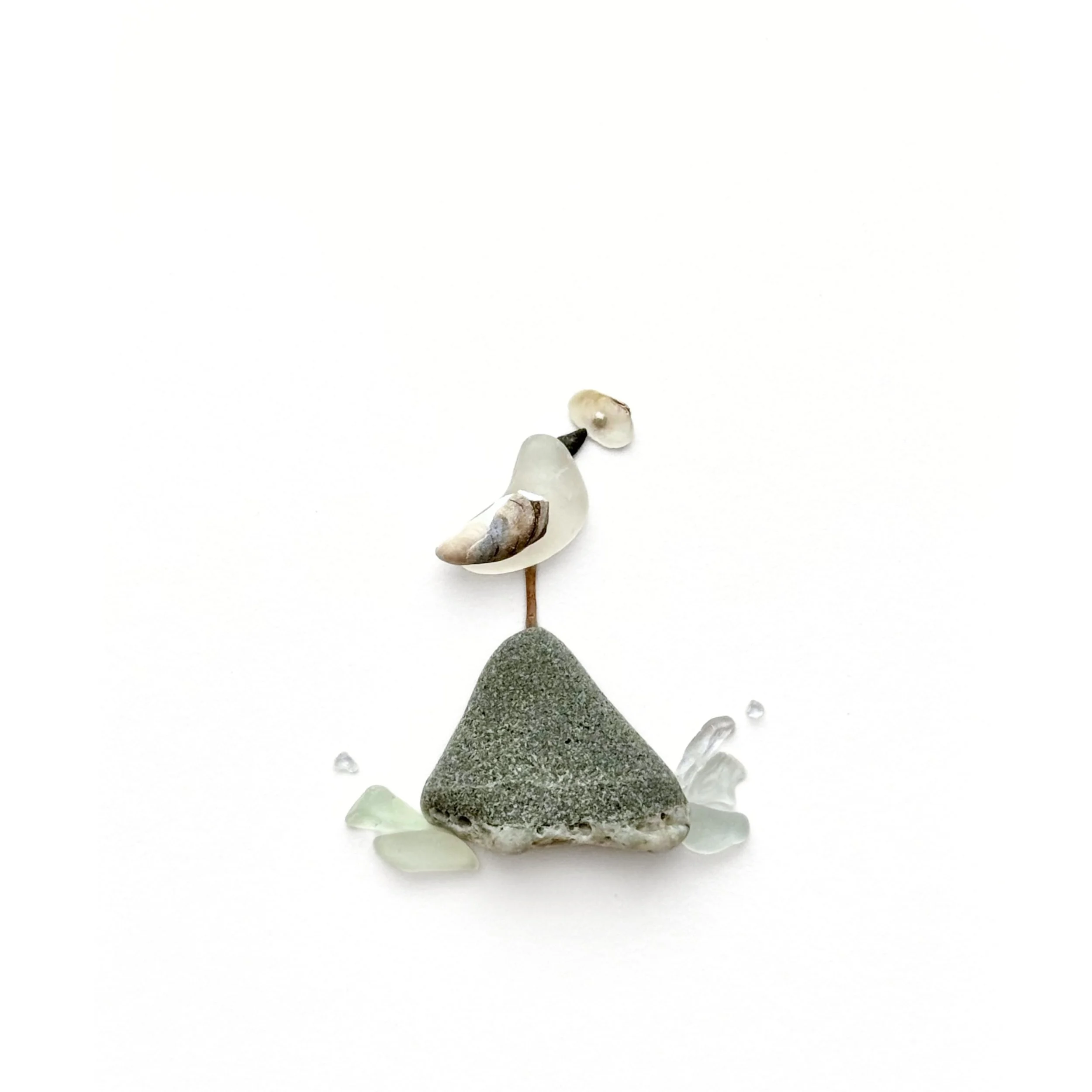 Original sea glass art featuring a small shorebird perched on a gray beach stone, holding a seashell, with pale aqua sea glass and coastal details below.Created with genuine Pacific Coast finds.
