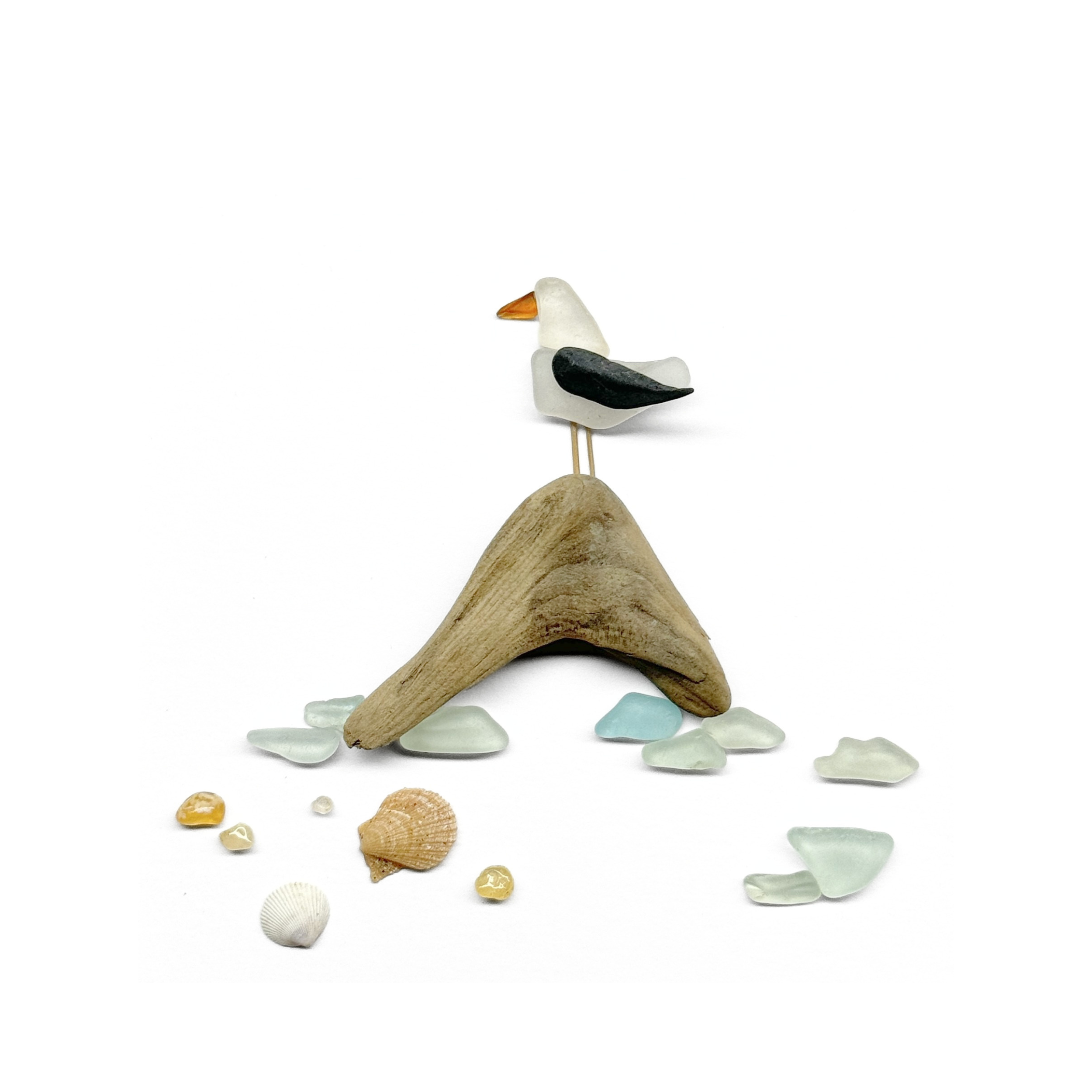 Coastal seabird perched on sculptural driftwood, surrounded by sea glass and tiny beach treasures.