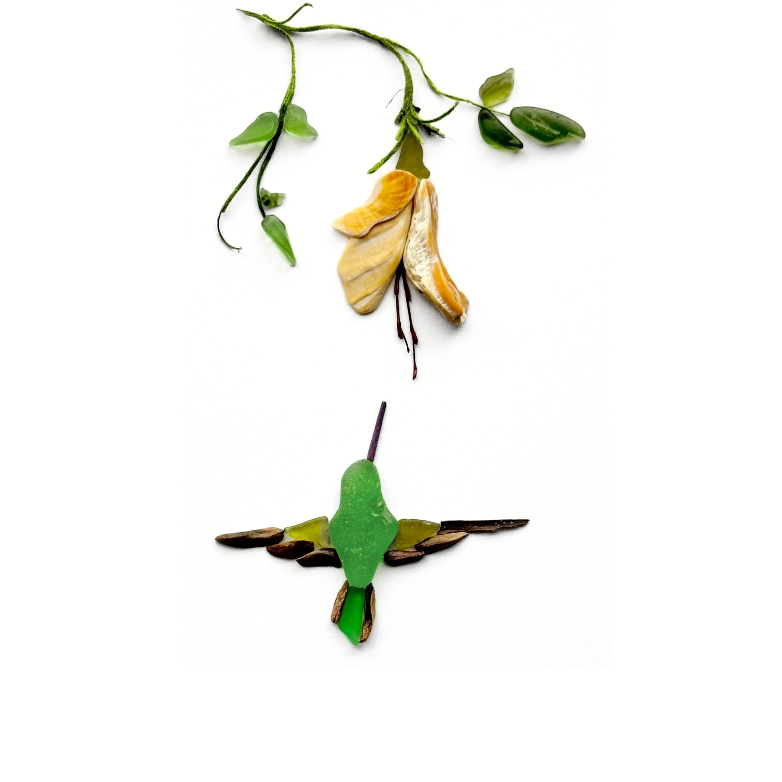 A hummingbird hovers beneath golden shell blossoms, created with naturally shaped sea glass, natural stems and coastal finds.