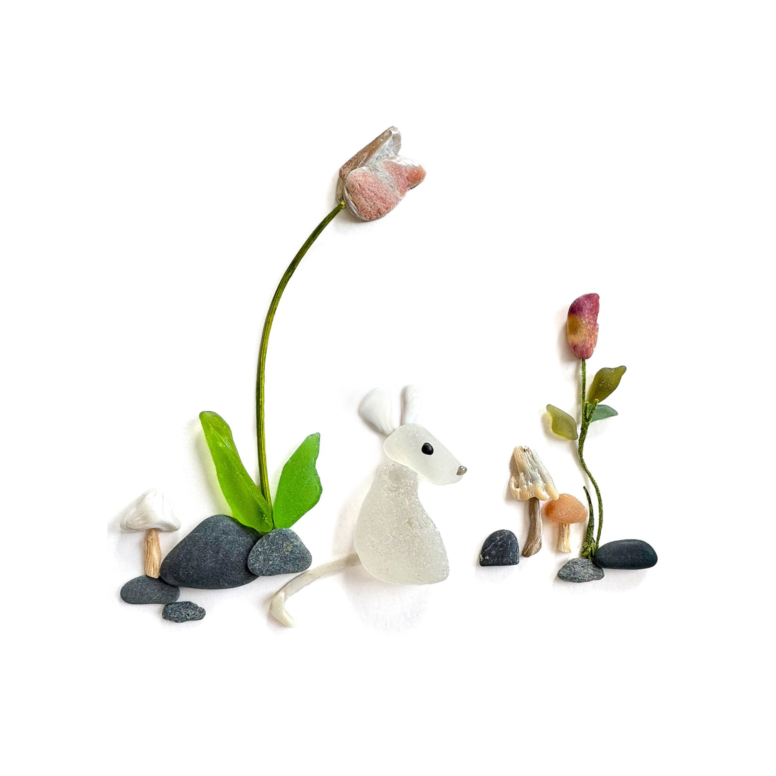 A white sea glass mouse sits among flowers, mushrooms, and other tiny woodland treasures.