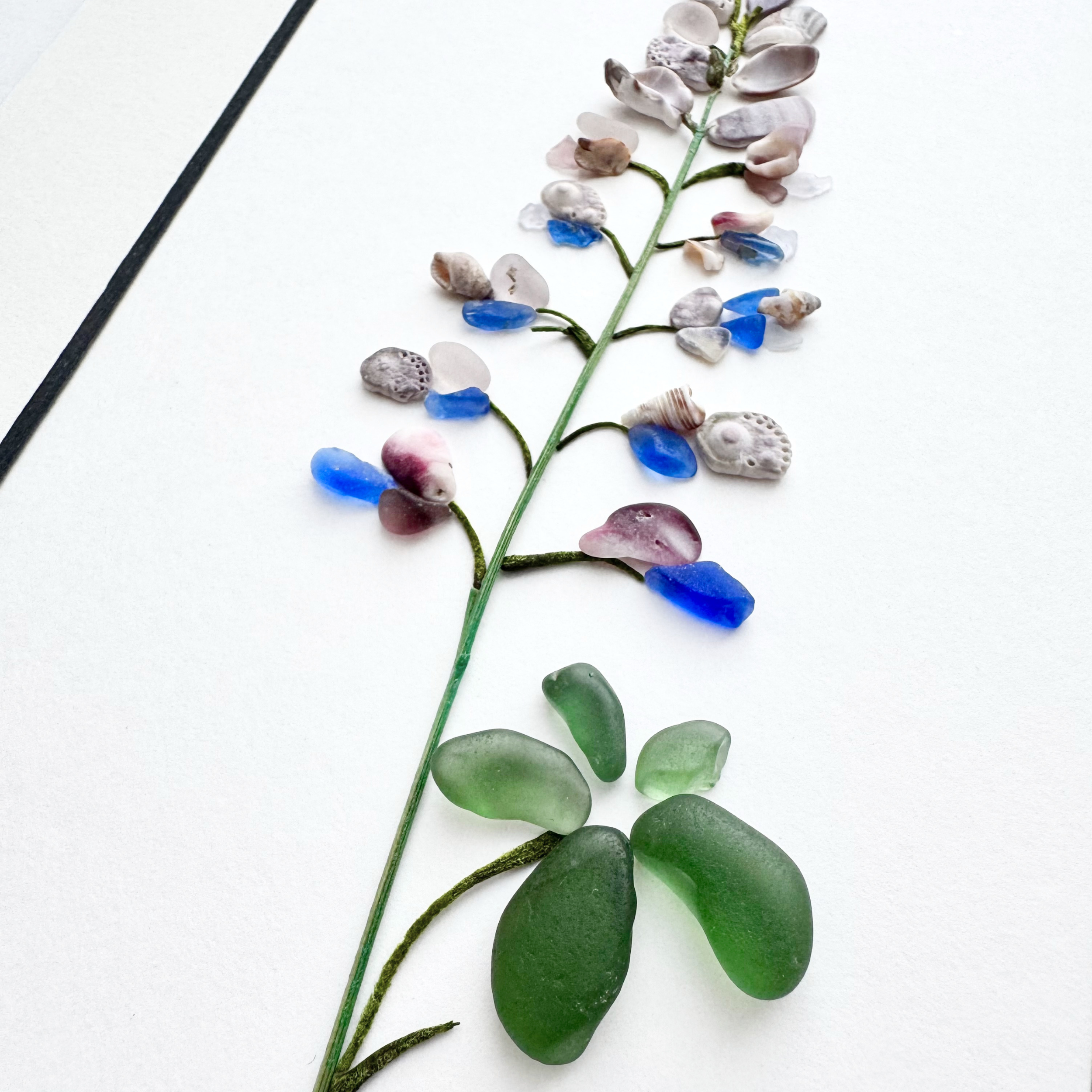 Close-up of a sea glass lupine with lavender shell petals, vivid blue accents, and green leaves.