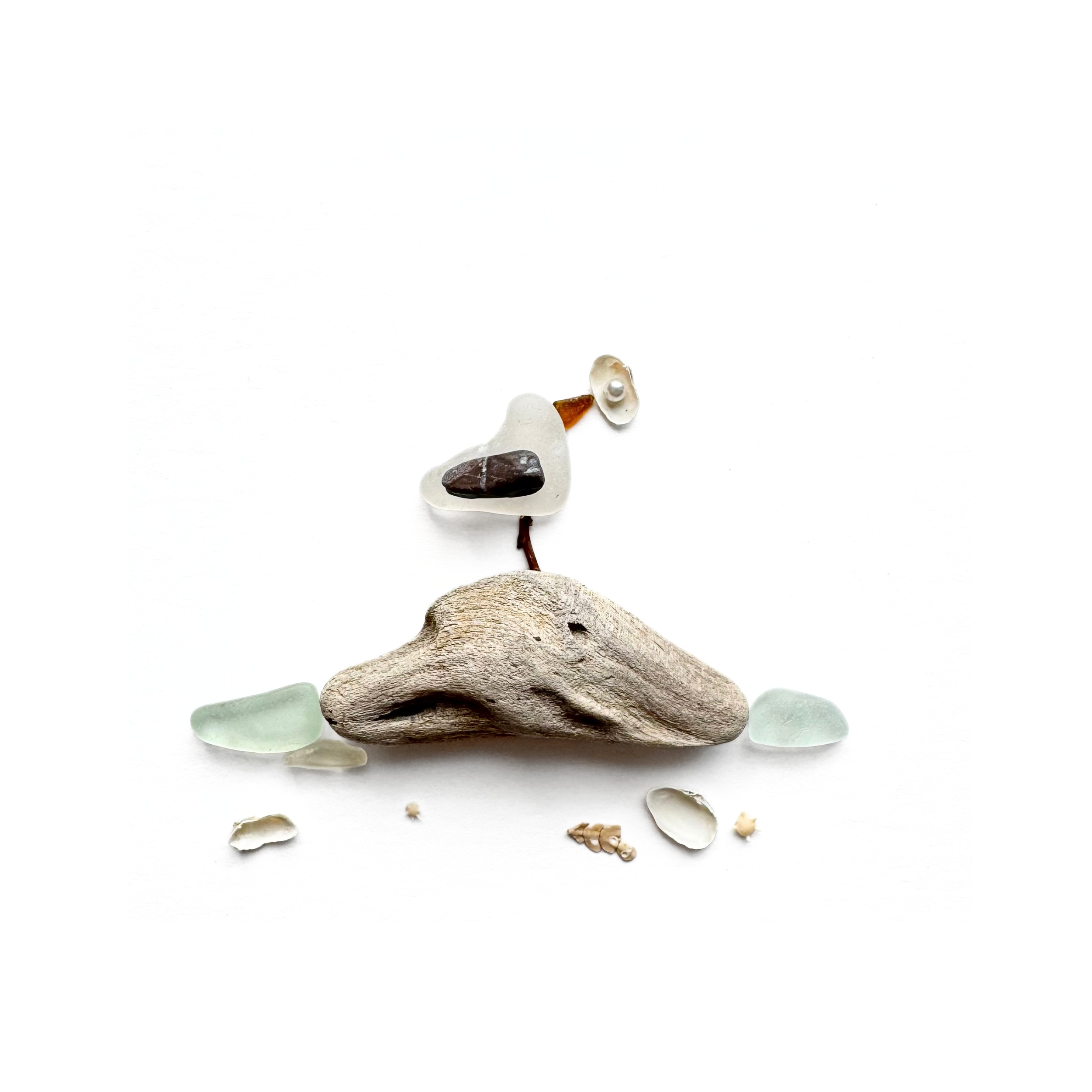 Tiny seabird holding shell perched on naturally weathered driftwood in an original sea glass coastal scene.