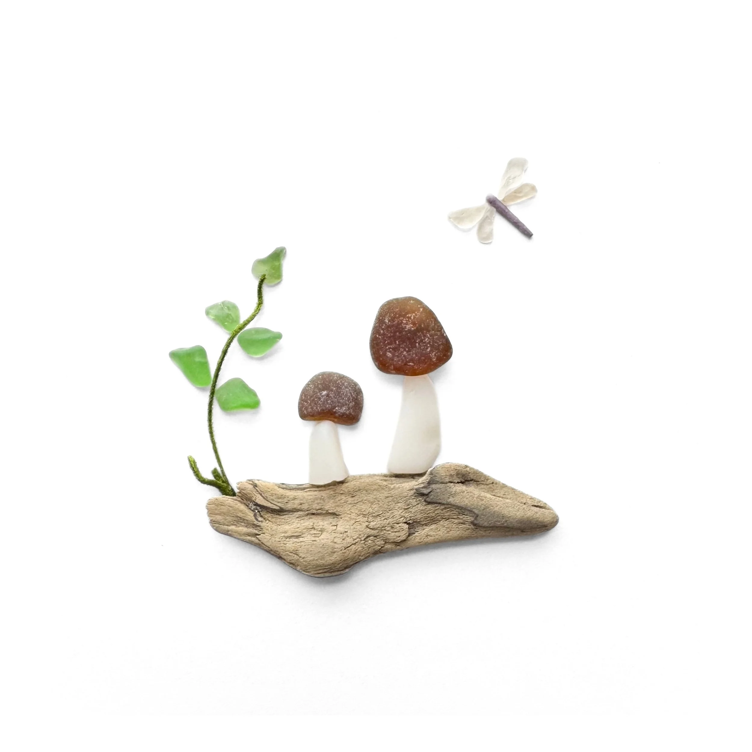 Original sea glass woodland artwork featuring two brown-capped mushrooms on weathered driftwood, green leaves, and a delicate dragonfly hovering above against a white background.