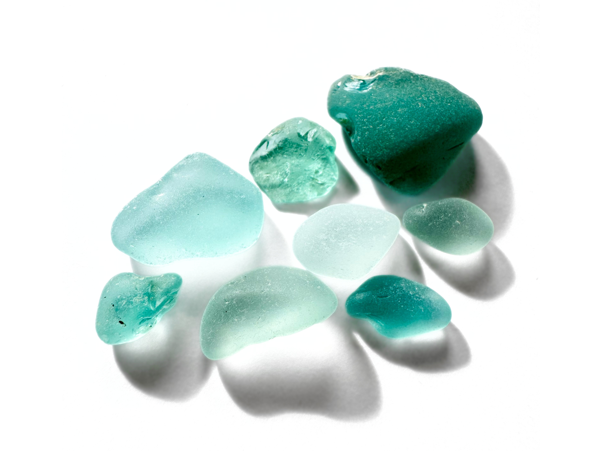 A small cluster of aqua and seafoam sea glass pieces on a white background