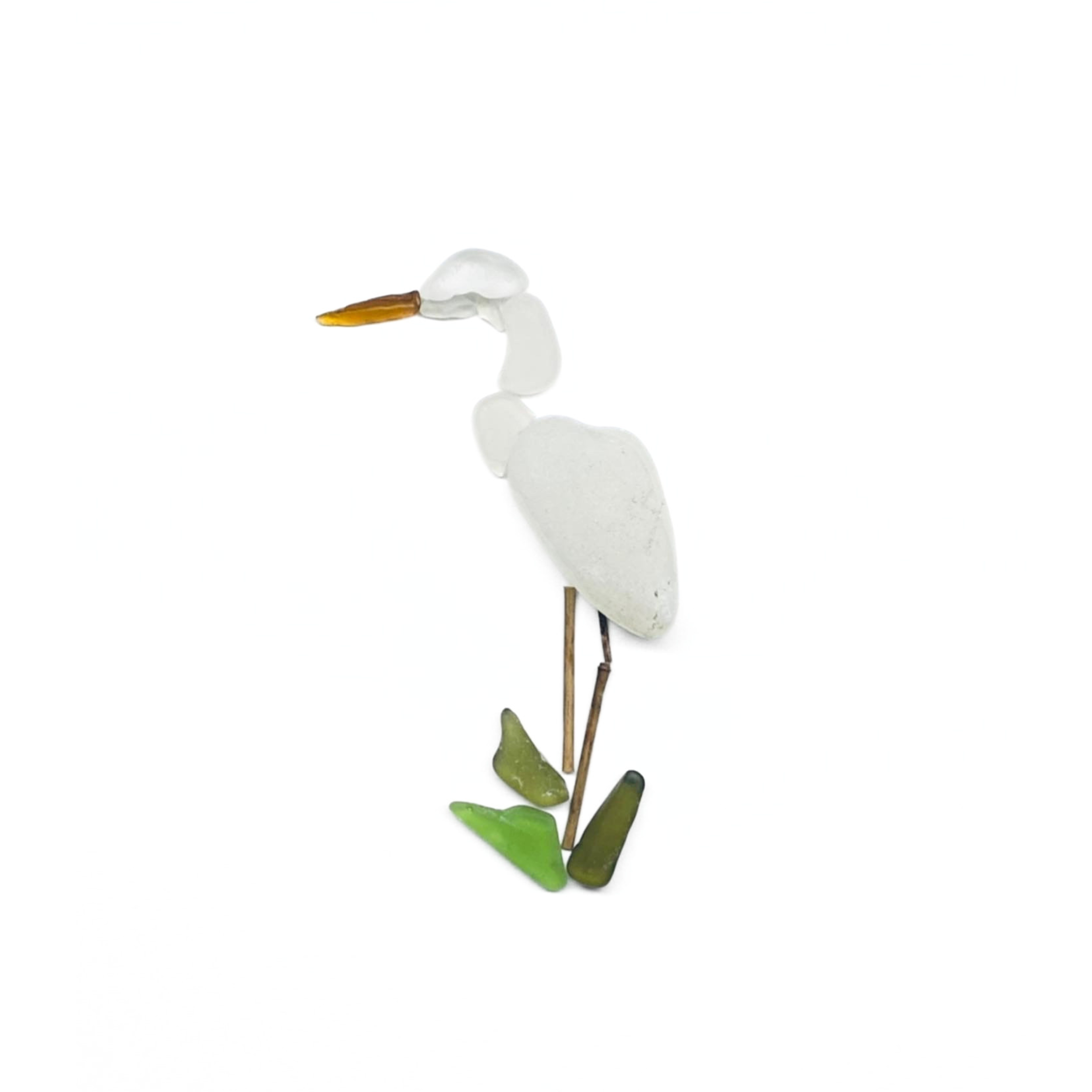 A graceful white sea glass egret stands among reeds, poised at the water’s edge.