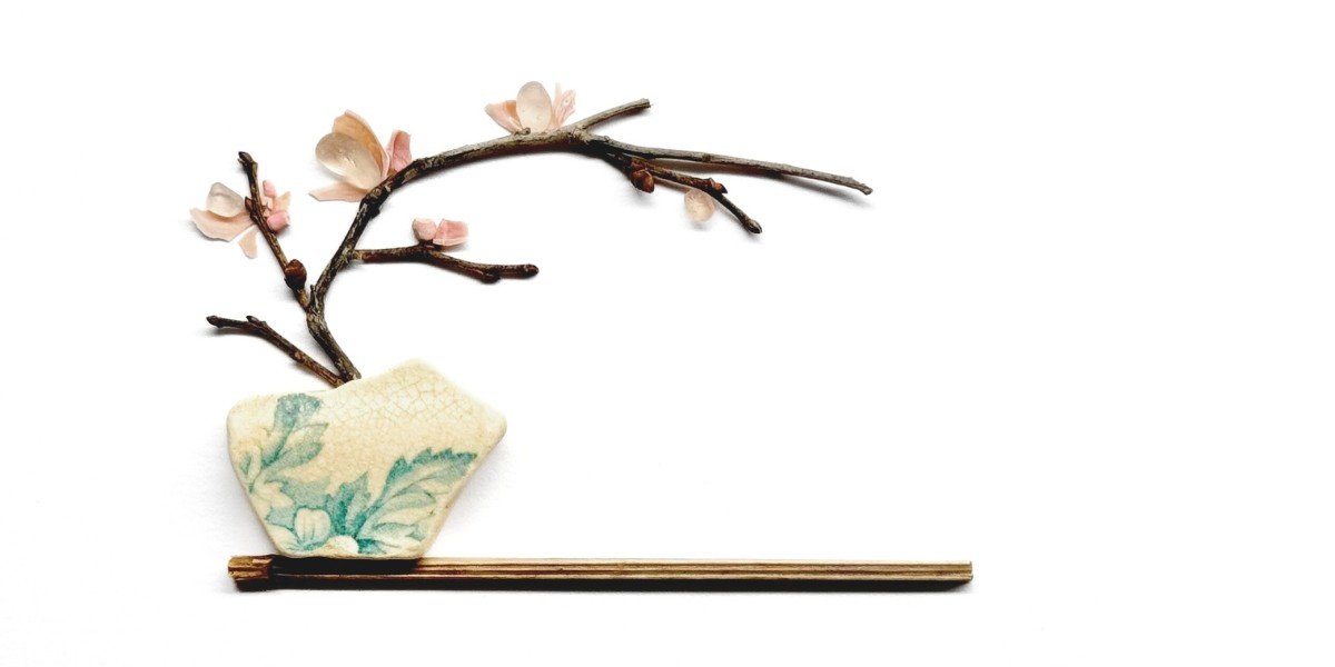 Minimalist sea glass artwork featuring a delicate cherry blossom branch with soft pink petals, a pottery shard vase, and natural driftwood base.