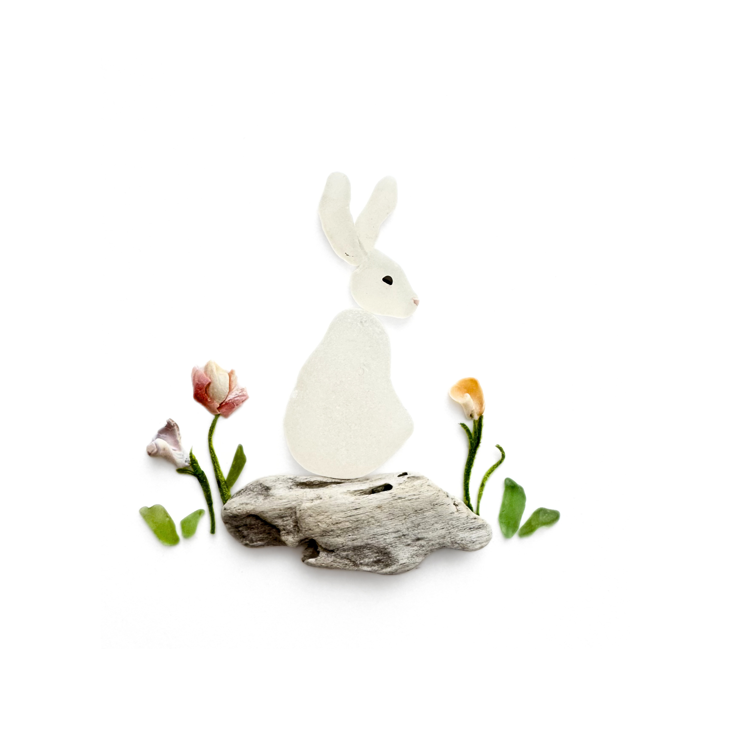 A white sea glass rabbit sits among wildflowers on a beautifully textured piece of driftwood.