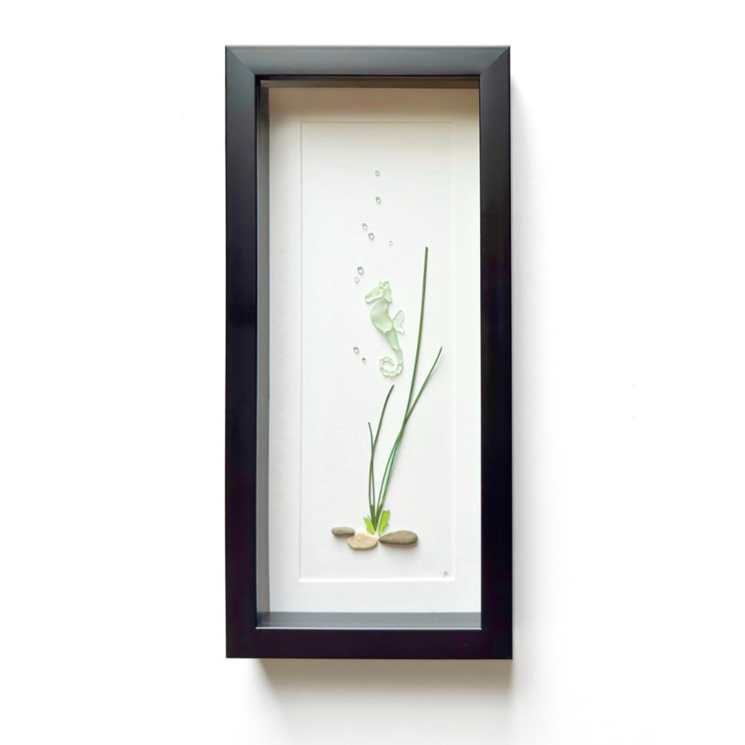 Framed aqua sea glass seahorse floating beside preserved seagrass in a tall black shadow box.