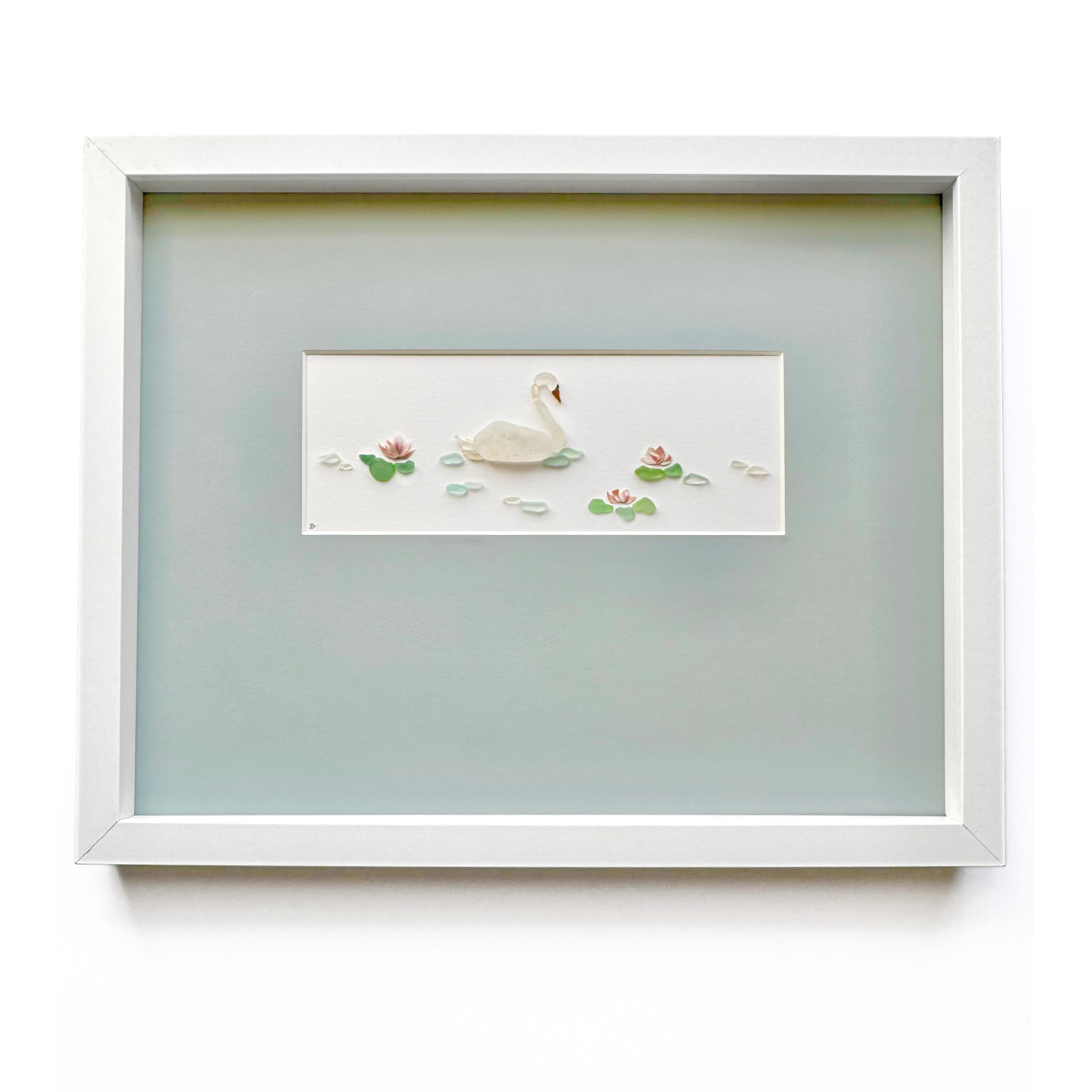 A framed white swan glides among delicate water lilies on a soft gray mat.