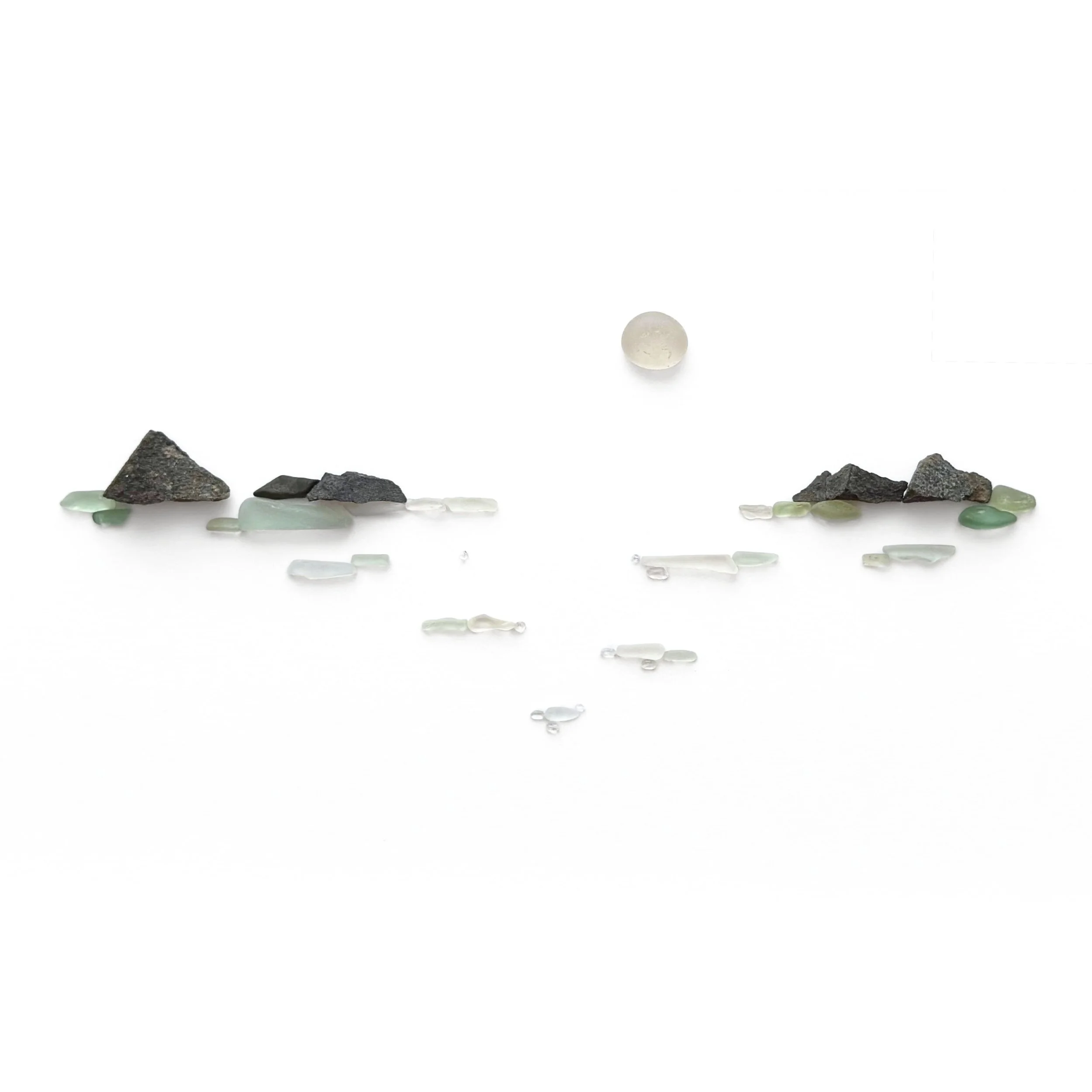 Original sea glass seascape artwork featuring a pale round moon above Pacific waters, dark beach stones forming rocky shores, and pale green and white sea glass suggesting gentle waves.