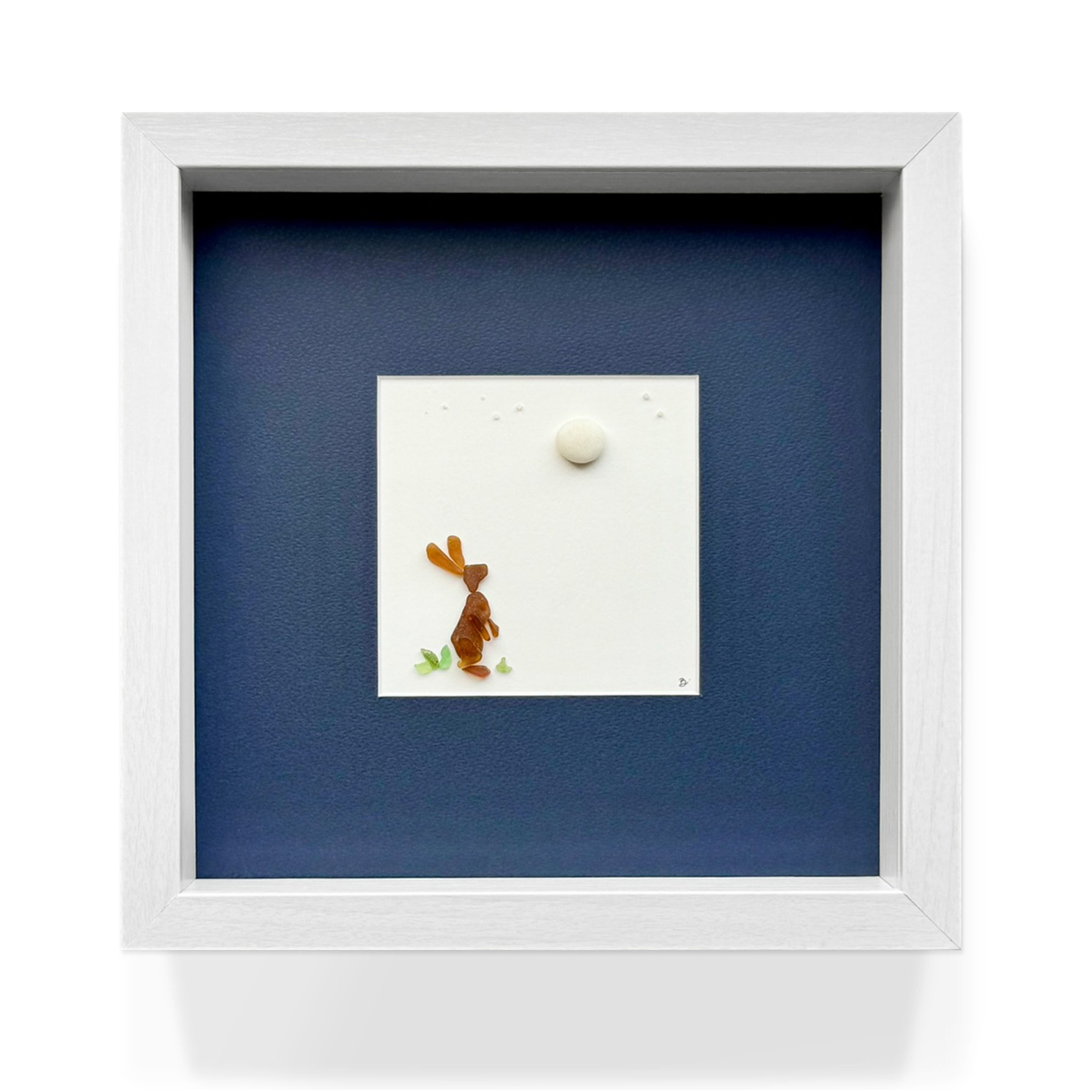 A framed view of a sea glass rabbit beneath the moon, set against a deep blue mat.