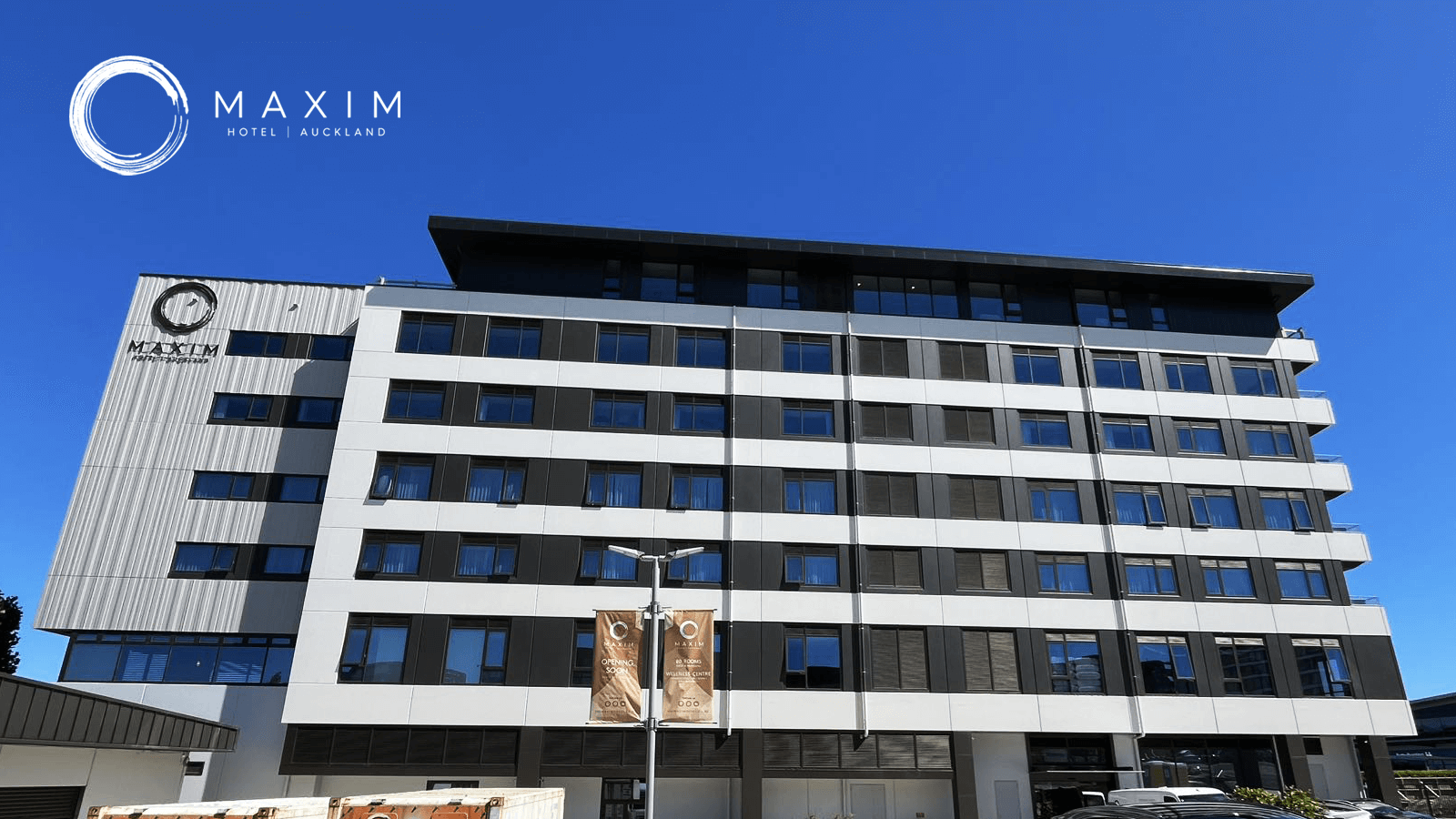 Modern multi-story hotel building with Maxlm Hotel logo, black and white exterior, and blue sky background.