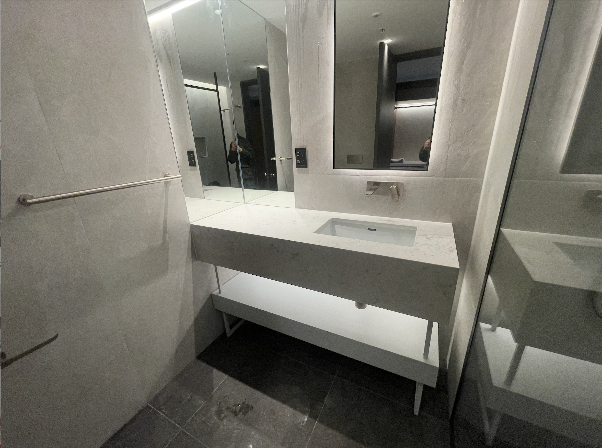 A modern bathroom with marble walls, black mirrors, a white sink, and a white towel rack. The photo is taken in a tilted angle, reflecting the person taking the picture in the mirrors.