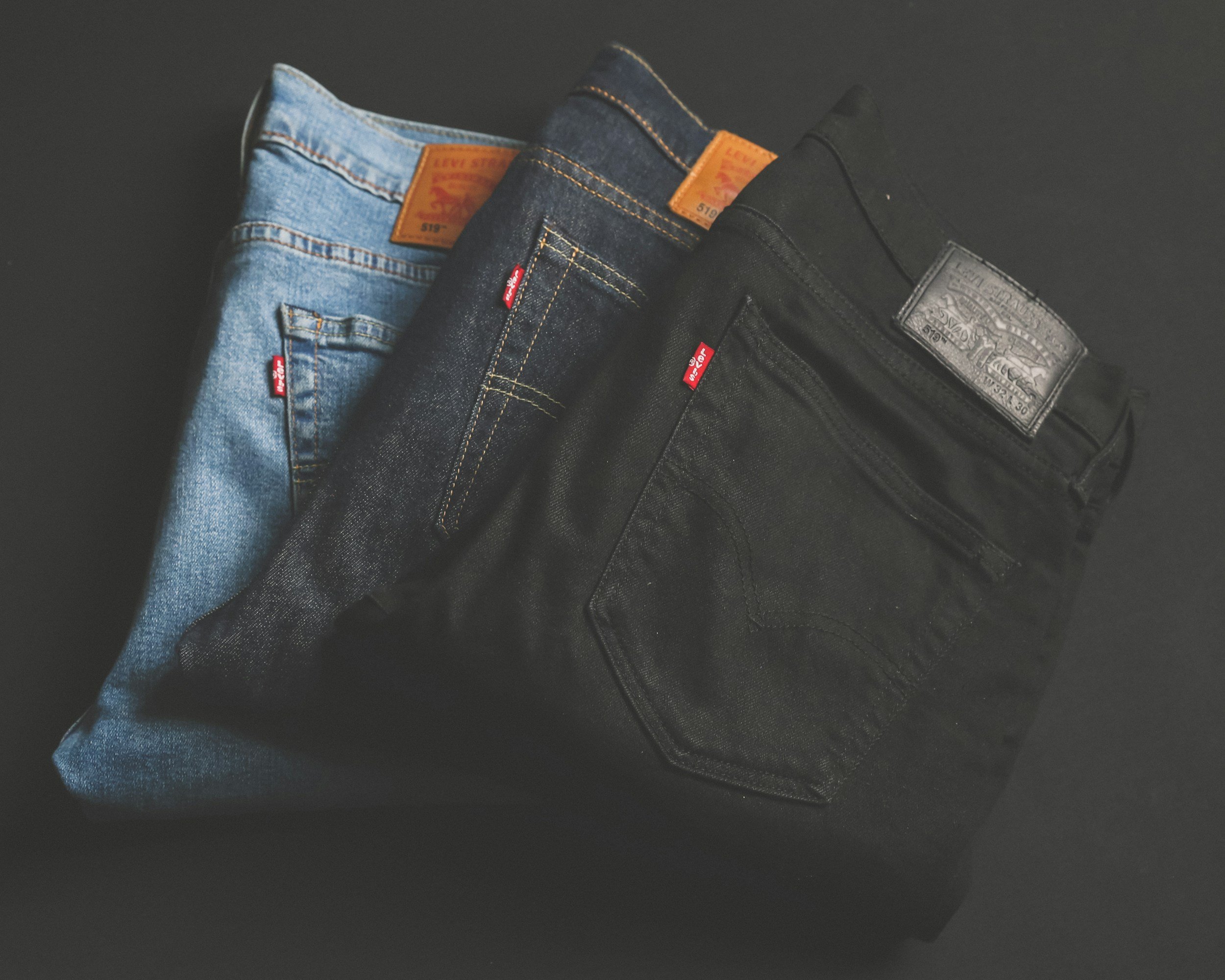 Three pairs of Levi's jeans in light blue, dark blue, and black, folded and placed on a dark surface. walking into fashion