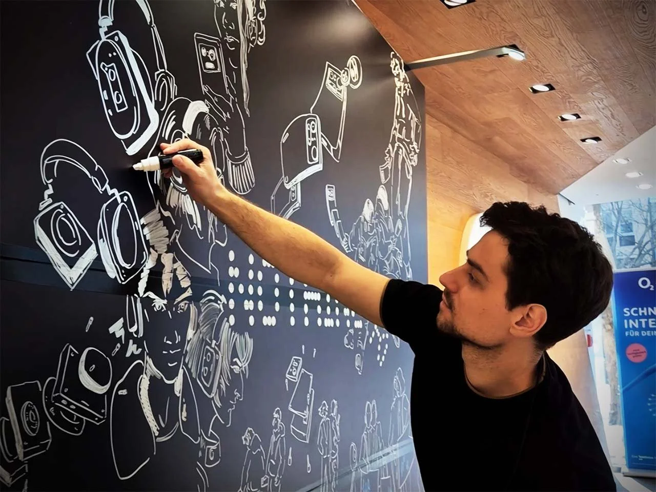 Eli Schneider, Live-Zeichner und Event-Illustrator, zeichnet mit weißem Marker eine große Illustrationen auf eine schwarze Tafel, während eines Events.