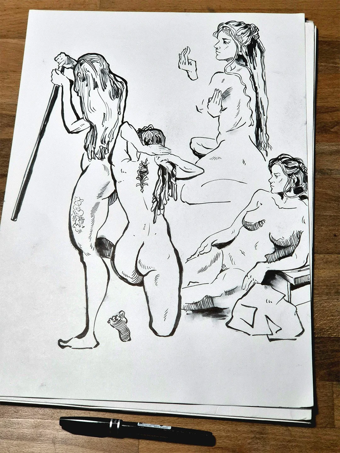 Tusche-Zeichnung von weiblichen Aktfiguren in verschiedenen Posen. Ein Stift liegt vor der Zeichnung.