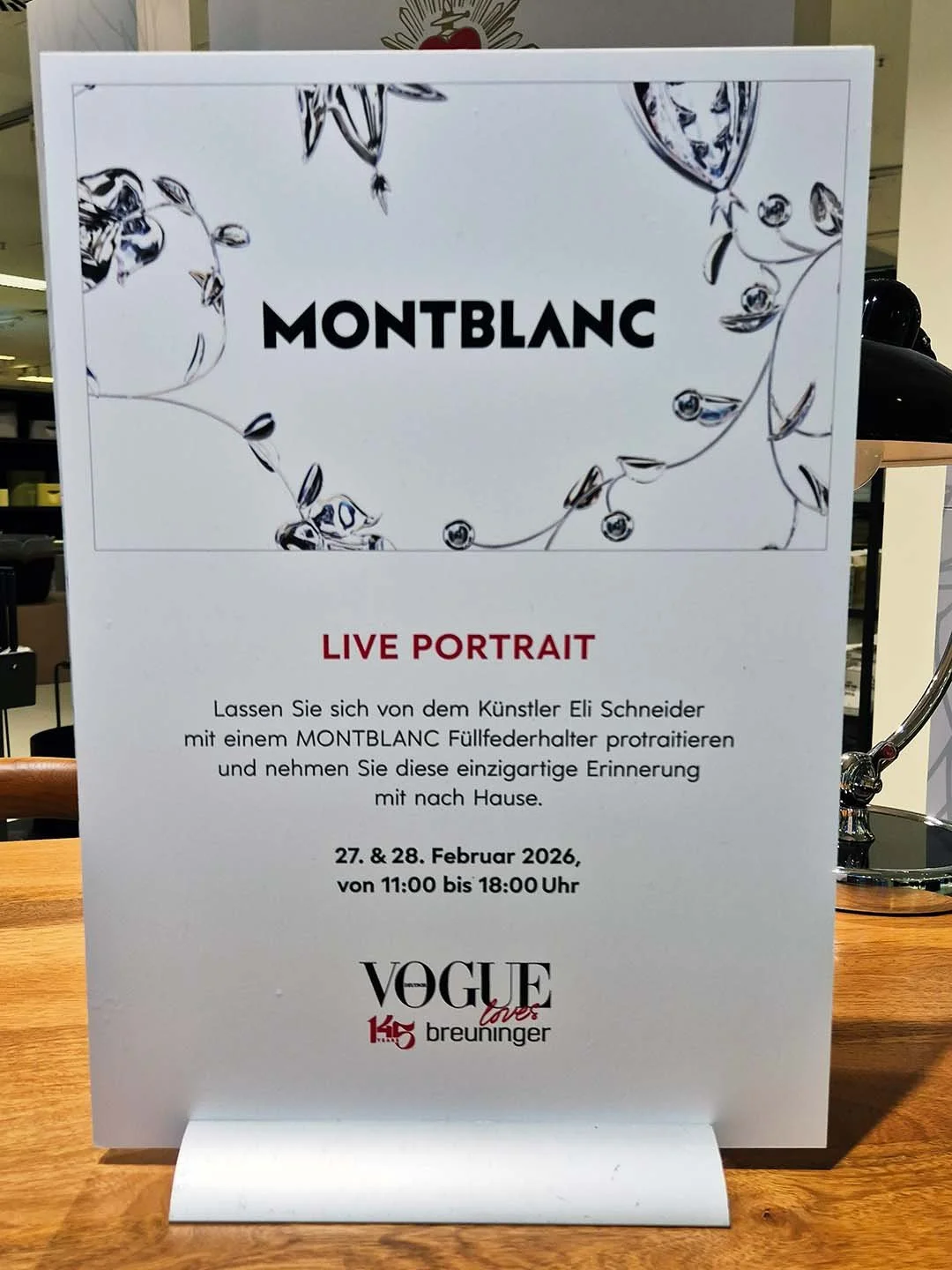 Ein Informationsplakat bewirbt eine Live-Portrait-Veranstaltung mit dem Künstler Eli Schneider, der am 27. und 28. Februar 2026 von 11:00 bis 18:00 Uhr stattfindet. Es wird eine Partnerschaft mit Montblanc hervorgehoben.