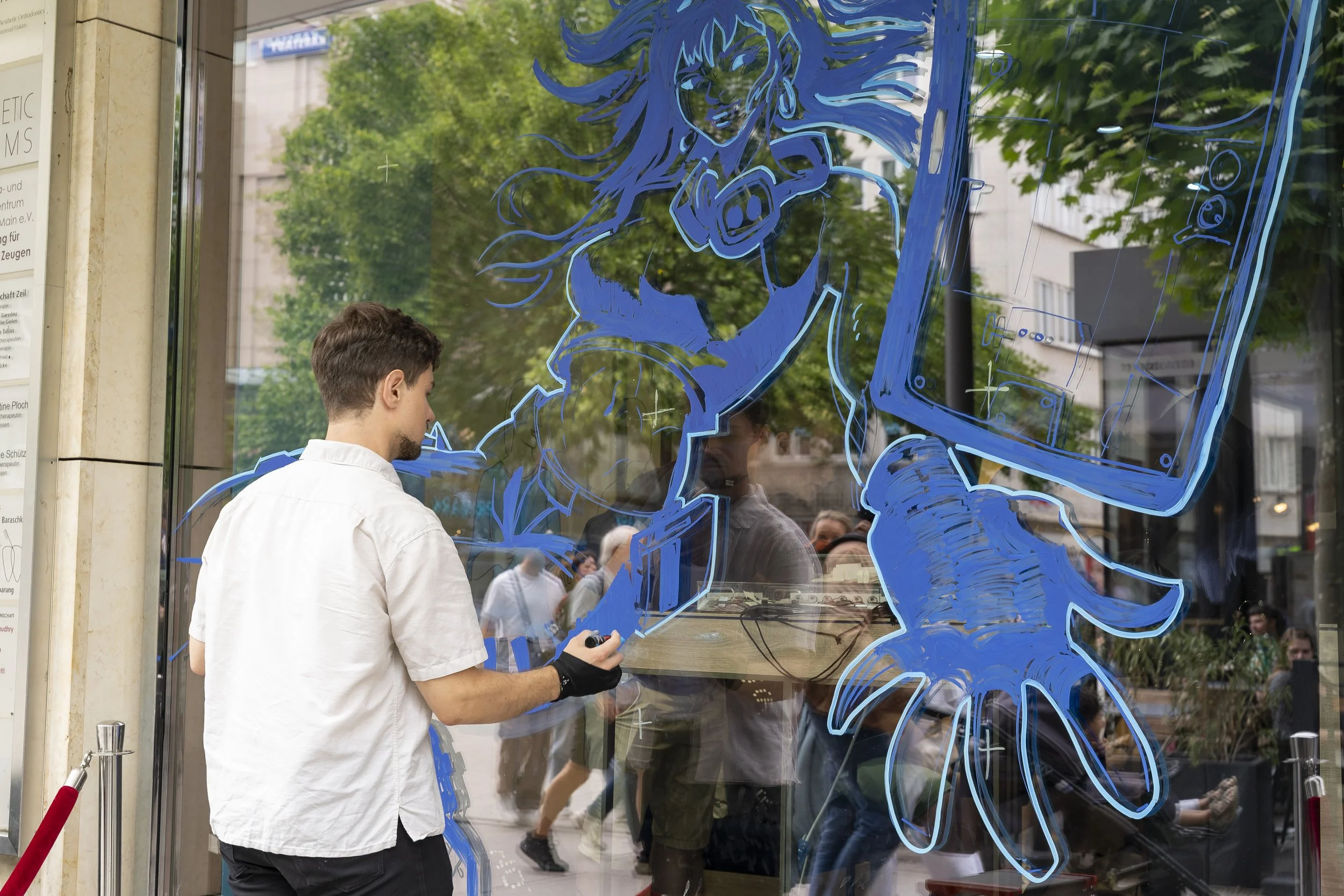Eli Schneider drawing a large blue graphic of a woman with long hair and a phone on the glass window outside a building.