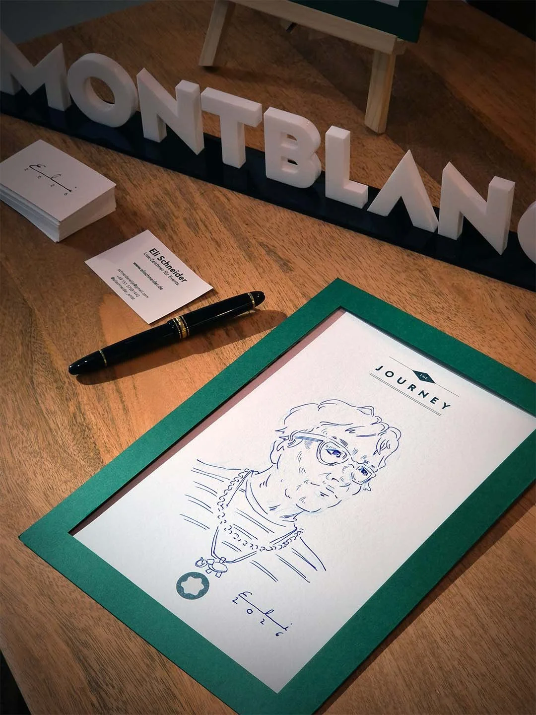 Eine handgezeichnete Karikatur einer älteren Frau mit Brille, auf einem weißen Blatt Papier, das in einem grünen Rahmen liegt. Im oberen Bereich steht in schwarzen Buchstaben 'THE JOURNEY'.