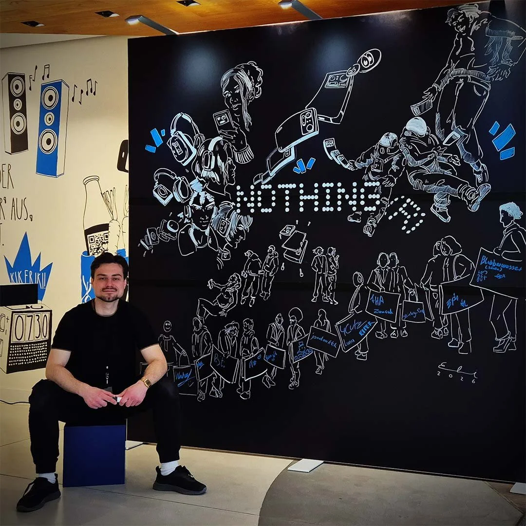 Ein Mann sitzt vor einer schwarzen Wand mit einer Streetart, die das Wort 'LOTHUNGE' in Lichterbuchstaben zeigt, umgeben von linienartigen Zeichnungen von Menschen, die mit Musik und Gesprächen beschäftigt sind, sowie anderen Skizzen und Texten.