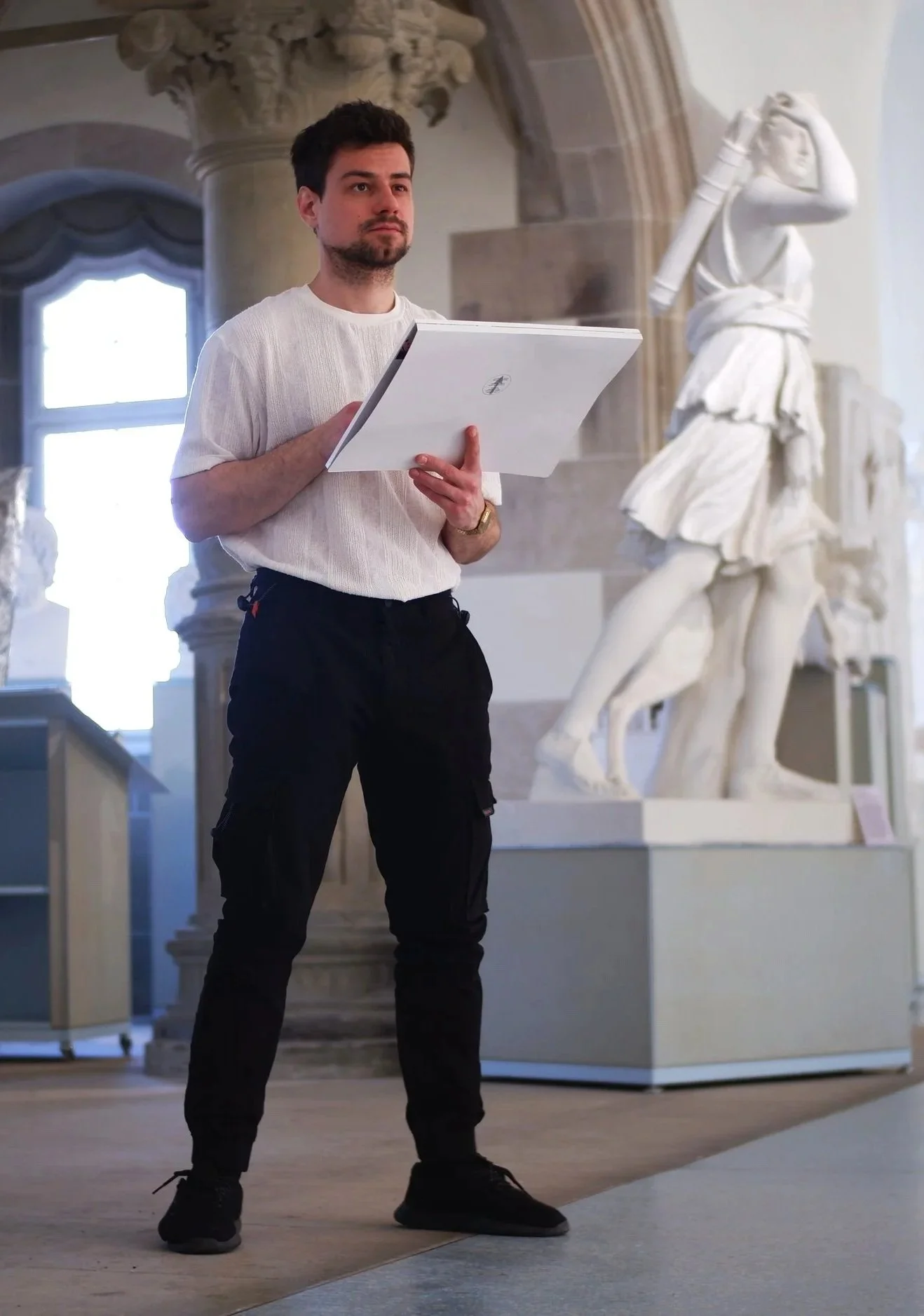 Männlicher Museumsführer mit Notizbuch in Hand im Museum mit Skulpturen im Hintergrund.
