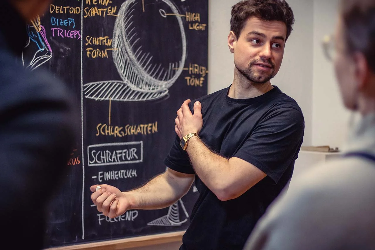 Eli Schneider unterrichtet Zeichnen an einer Tafel mit Diagrammen und Text über Licht und Schatten, während andere Personen ihm zuhören.